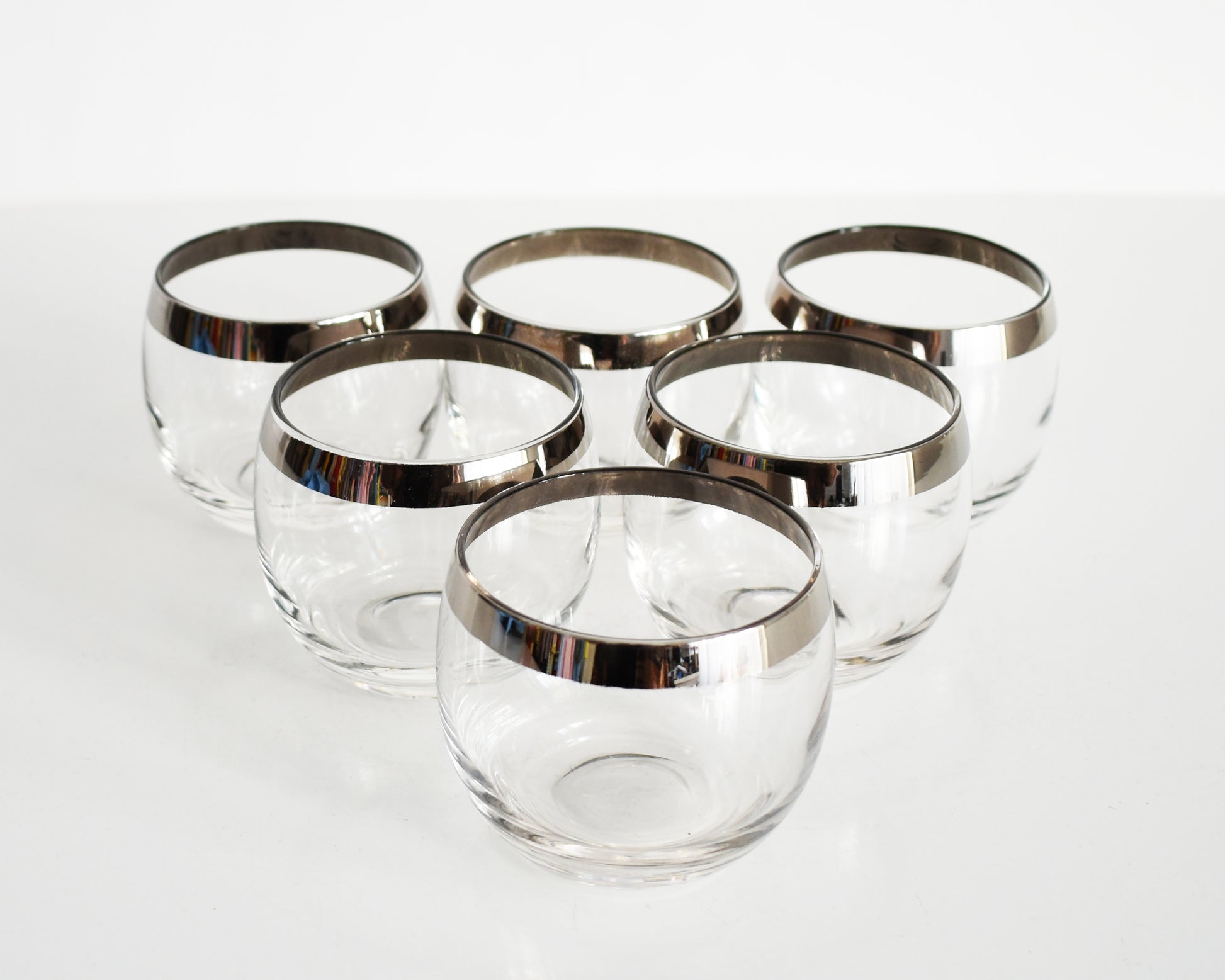An overhead shot of a set of six mid century roly poly glasses with silver rims. 