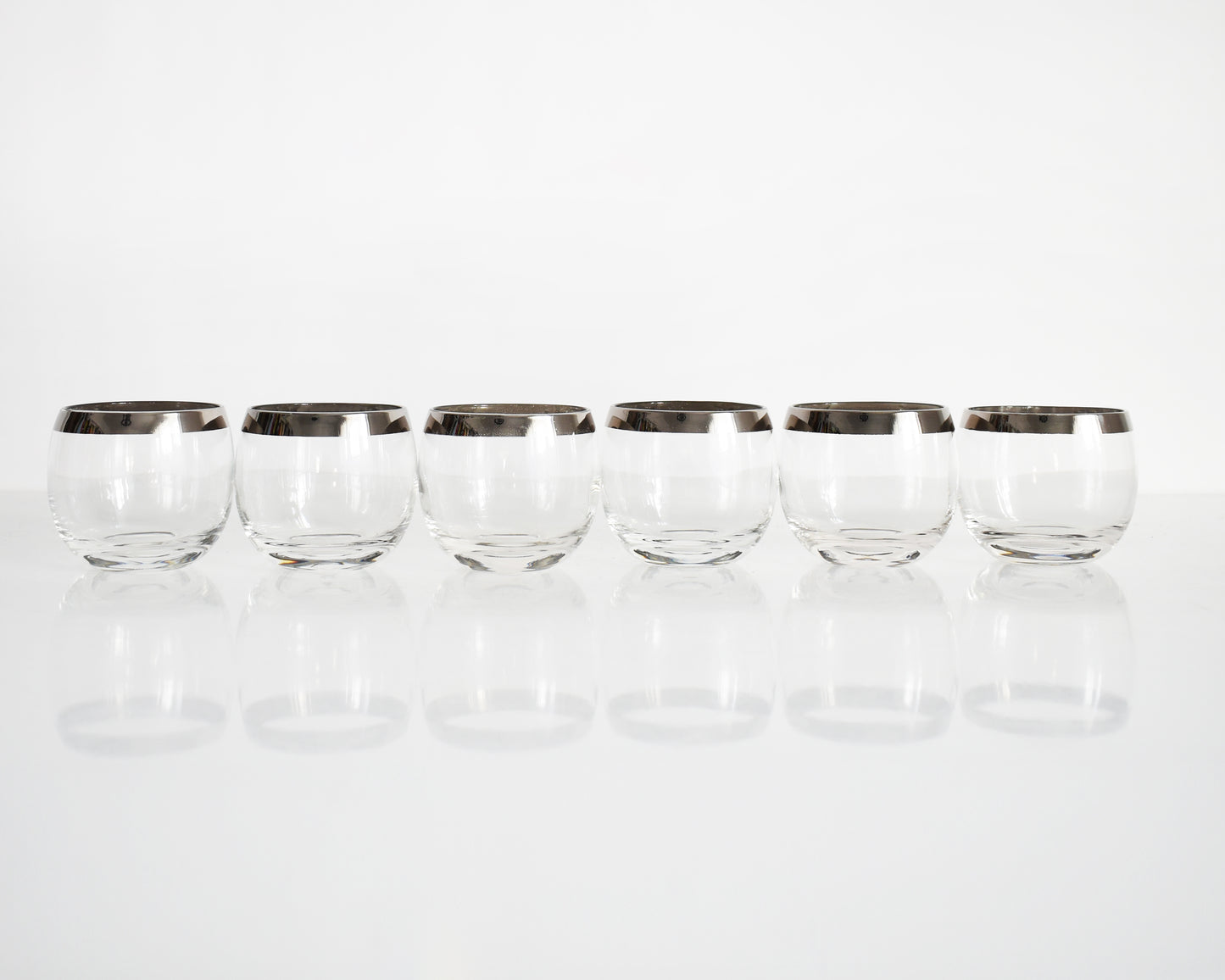 A set of six mid century roly poly glasses with silver rims in a row