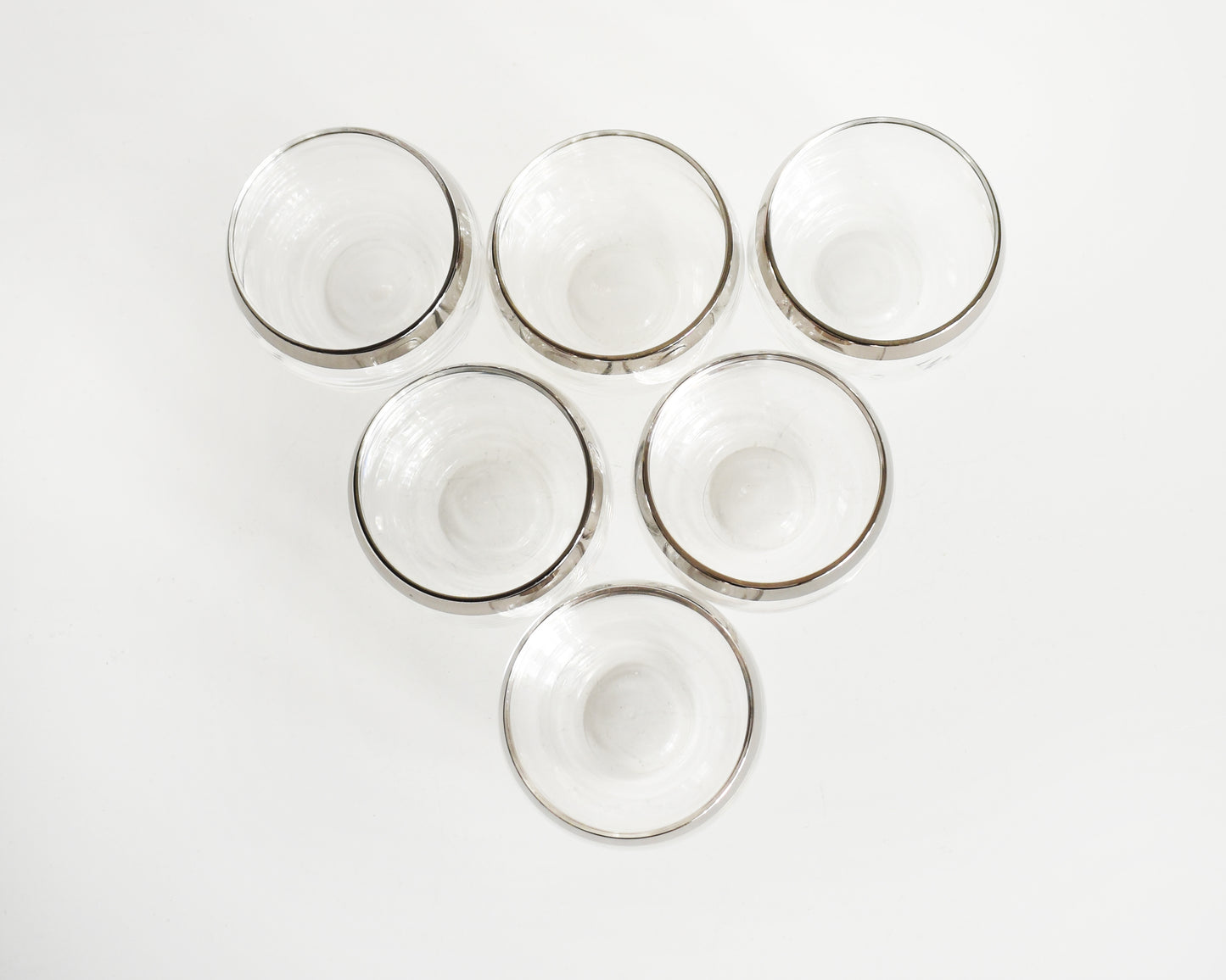 An overhead shot of a set of six mid century roly poly glasses with silver rims. 