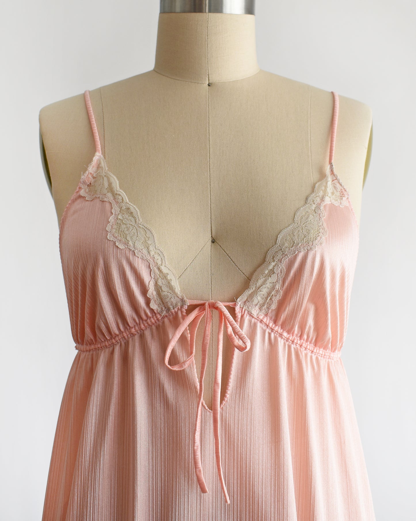 Close up of the bodice of a vintage 1970s peachy pink nightgown that has lace trim and a keyhole tie cutout