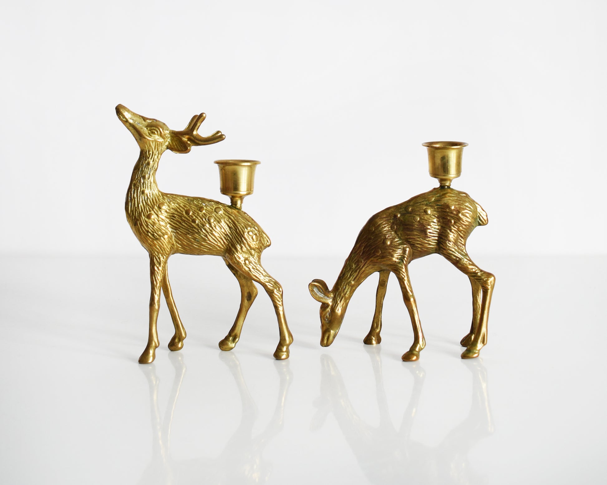 Vintage pair of brass deer figurine candle holders. The buck is standing upright displaying his antlers and the doe is grazing on the ground.