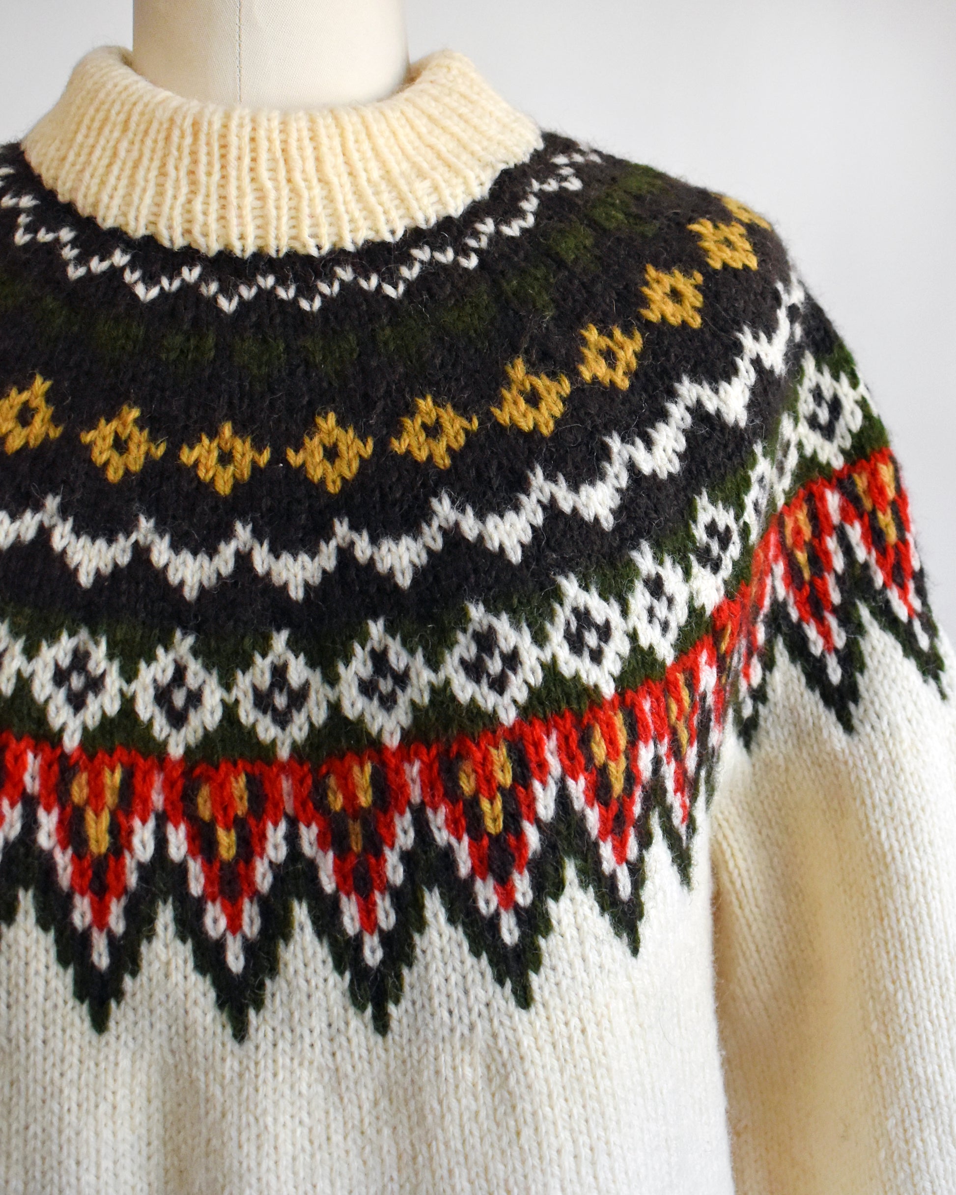 Close up of a vintage 1970s cream wool Nordic sweater with a brown, dark green, yellow, and red orange Fair Isle pattern around the collar.