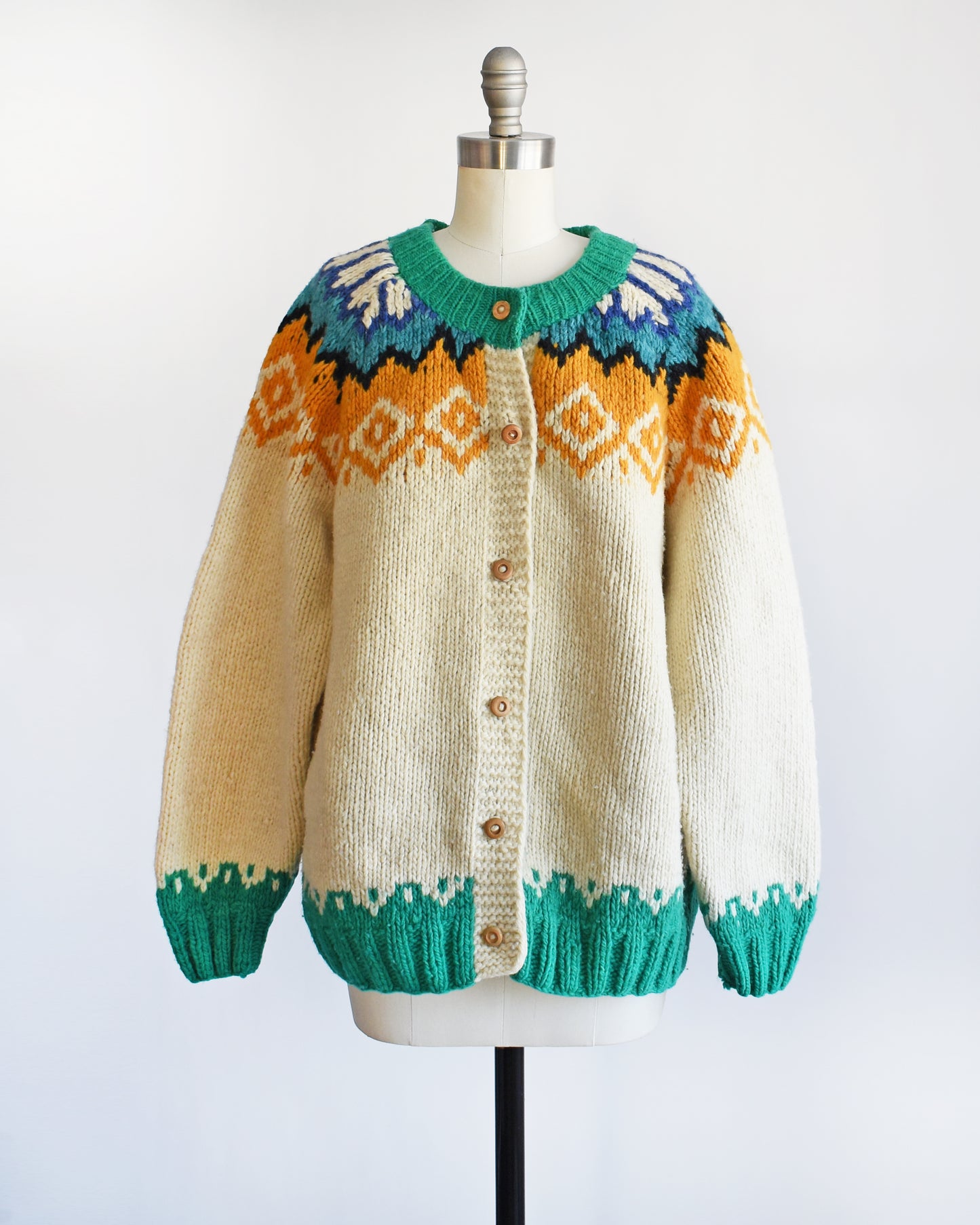 A vintage 1970s cream wool cardigan with bright green, dark blue, light blue, black, cream, and light orange Fair Isle pattern around the collar, and wood buttons on the front.