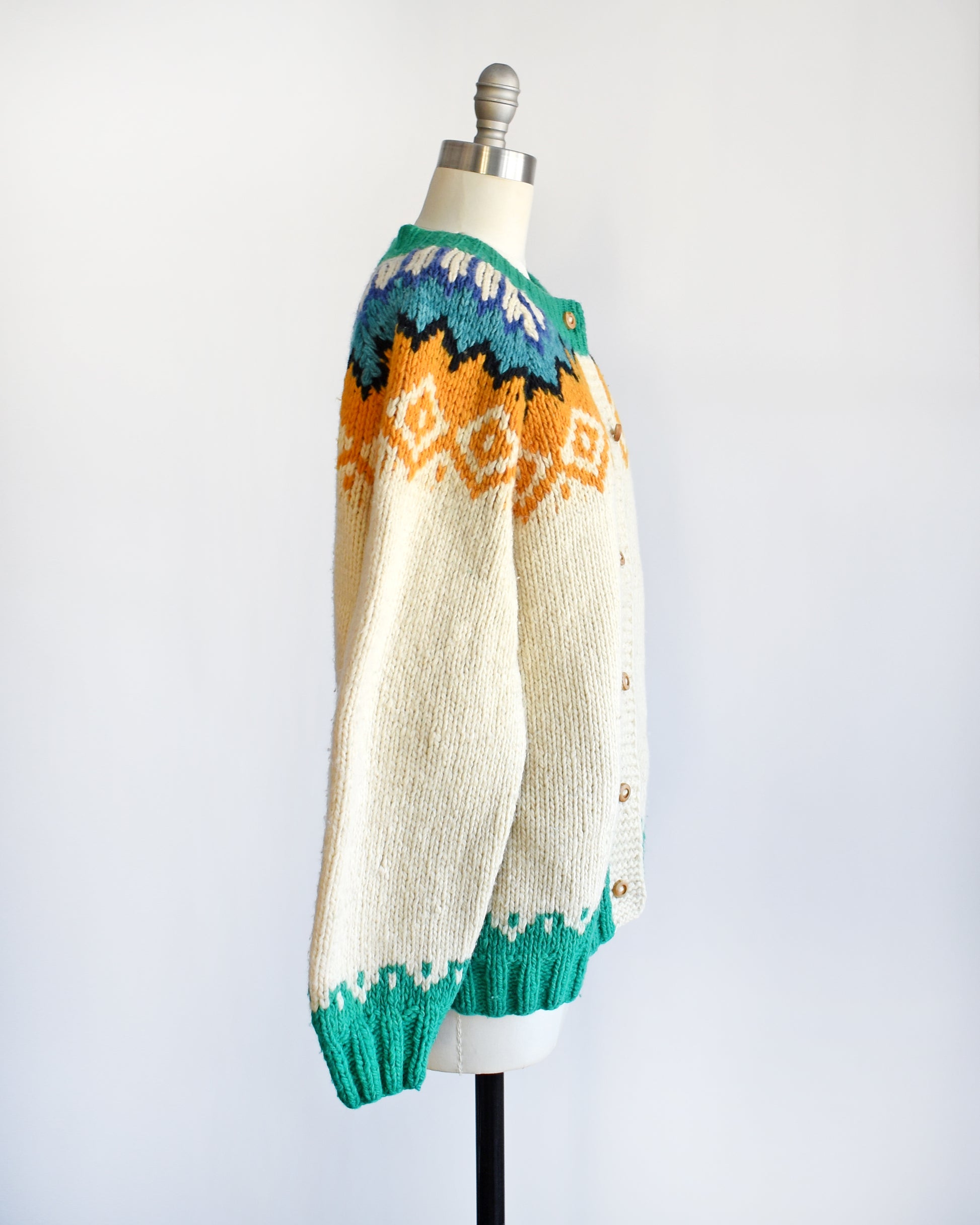 Side view of a vintage 1970s cream wool cardigan with bright green, dark blue, light blue, black, cream, and light orange Fair Isle pattern around the collar, and wood buttons on the front.