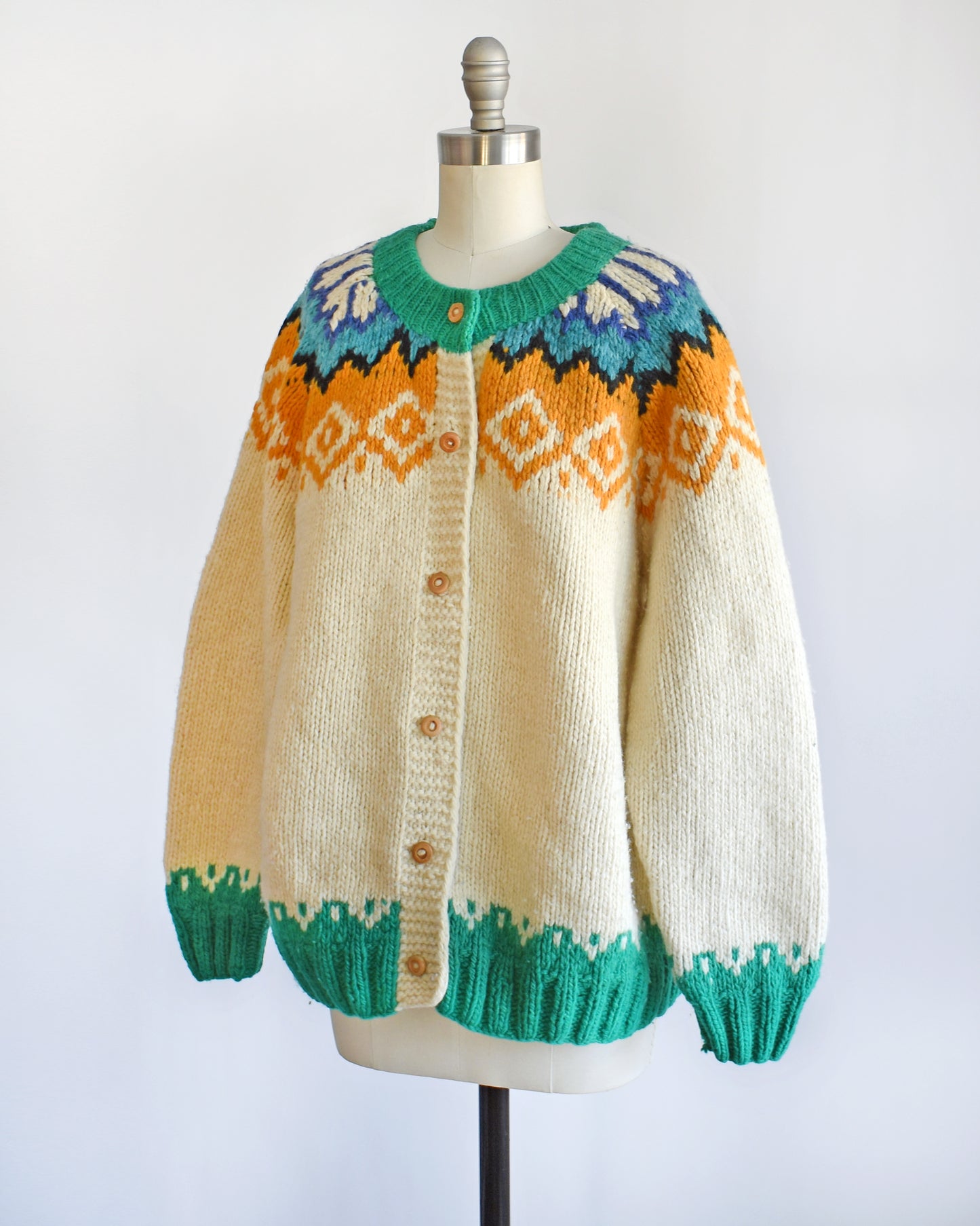 Side front view of a vintage 1970s cream wool cardigan with bright green, dark blue, light blue, black, cream, and light orange Fair Isle pattern around the collar, and wood buttons on the front.