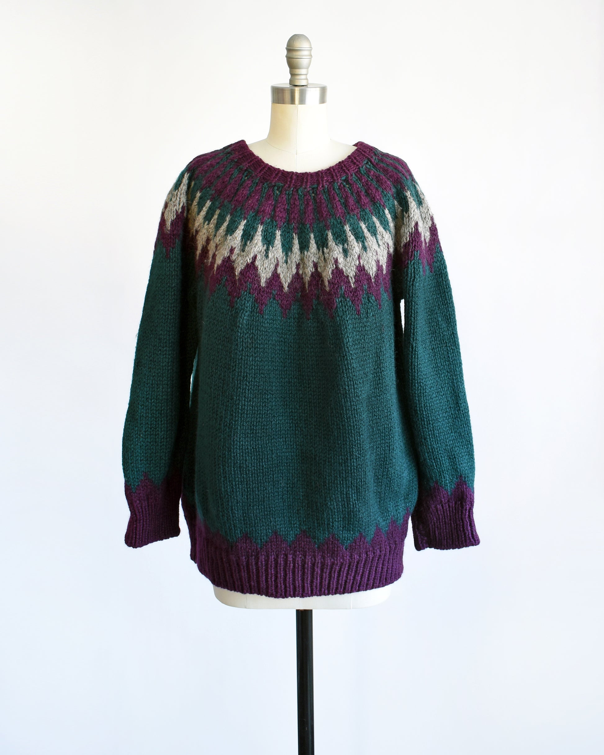 A vintage 1970s dark teal wool Nordic sweater with a purple and gray Fair Isle pattern around the collar. Complimentary purple pattern on the hem and cuffs.