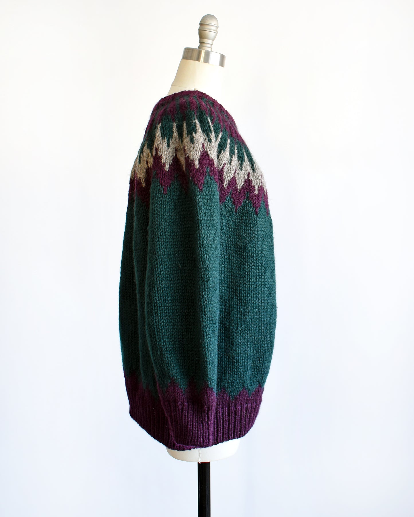 Side view of a vintage 1970s dark teal wool Nordic sweater with a purple and gray Fair Isle pattern around the collar. Complimentary purple pattern on the hem and cuffs.