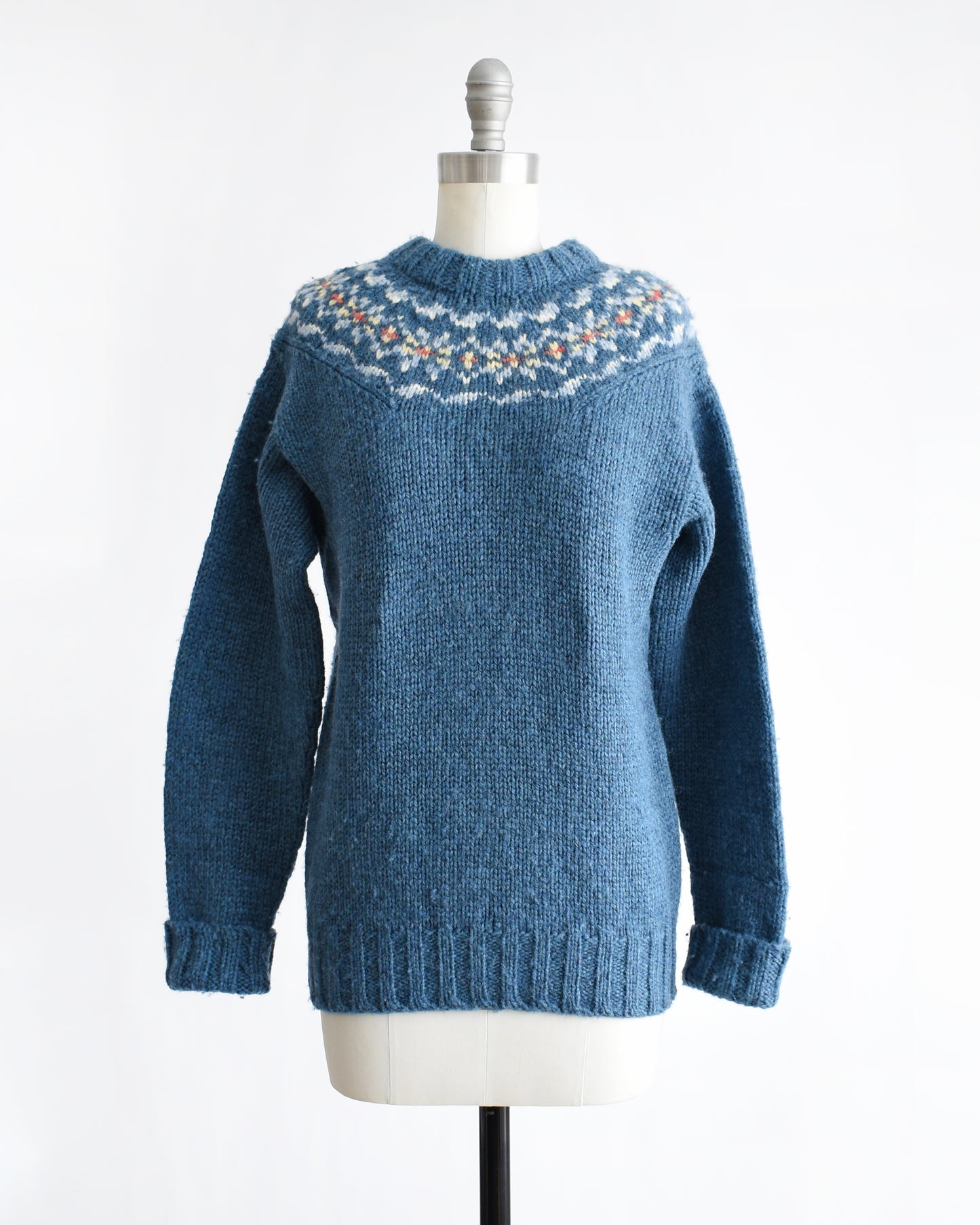 a vintage 1970s blue knitted sweater with patterned yoke on a mannequin against a white background