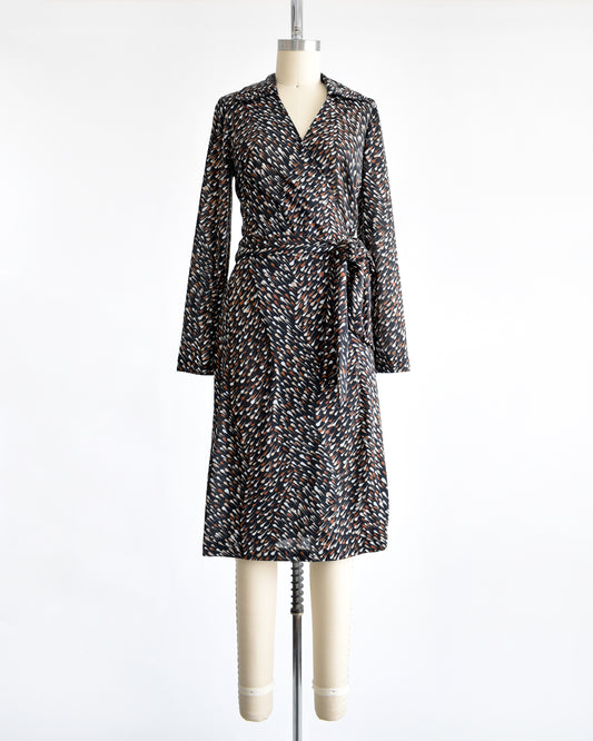 A vintage 1970s black wrap dress that has brown and white drop print, tie waist, and long sleeves.