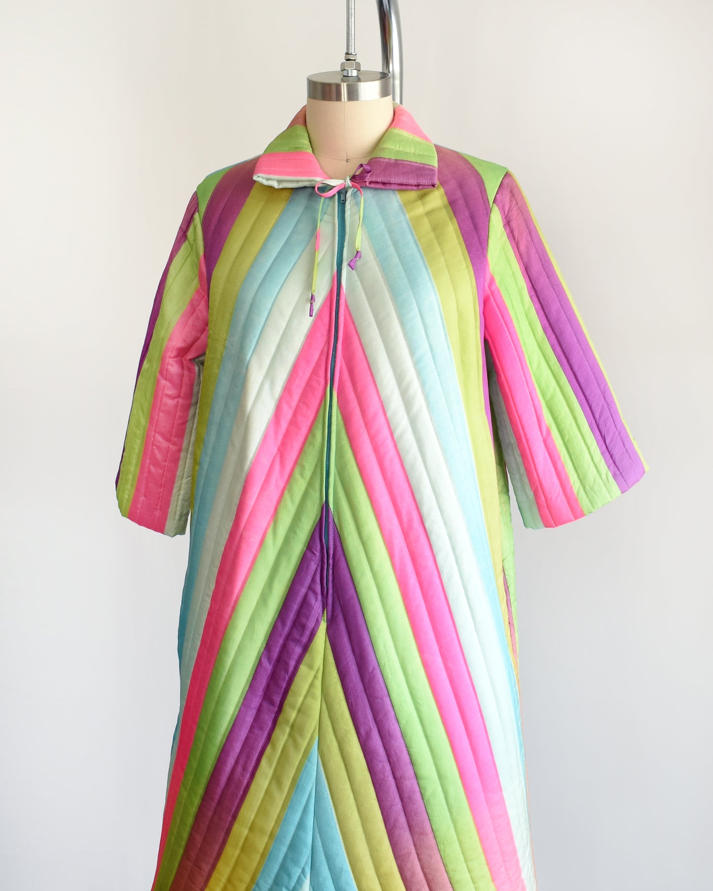Side front view of a vintage 1960s rainbow striped quilted robe with  purple, pink, blue, and green stripes
