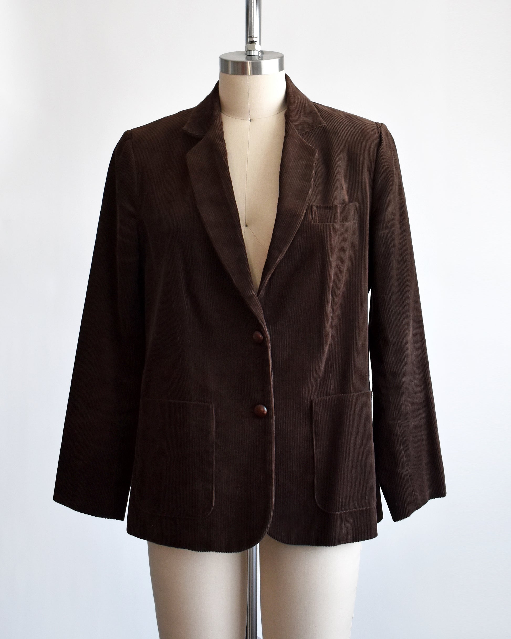 A vintage 1970s chocolate brown corduroy blazer features two faux wood plastic buttons on the front and two smaller matching buttons on the cuffs.