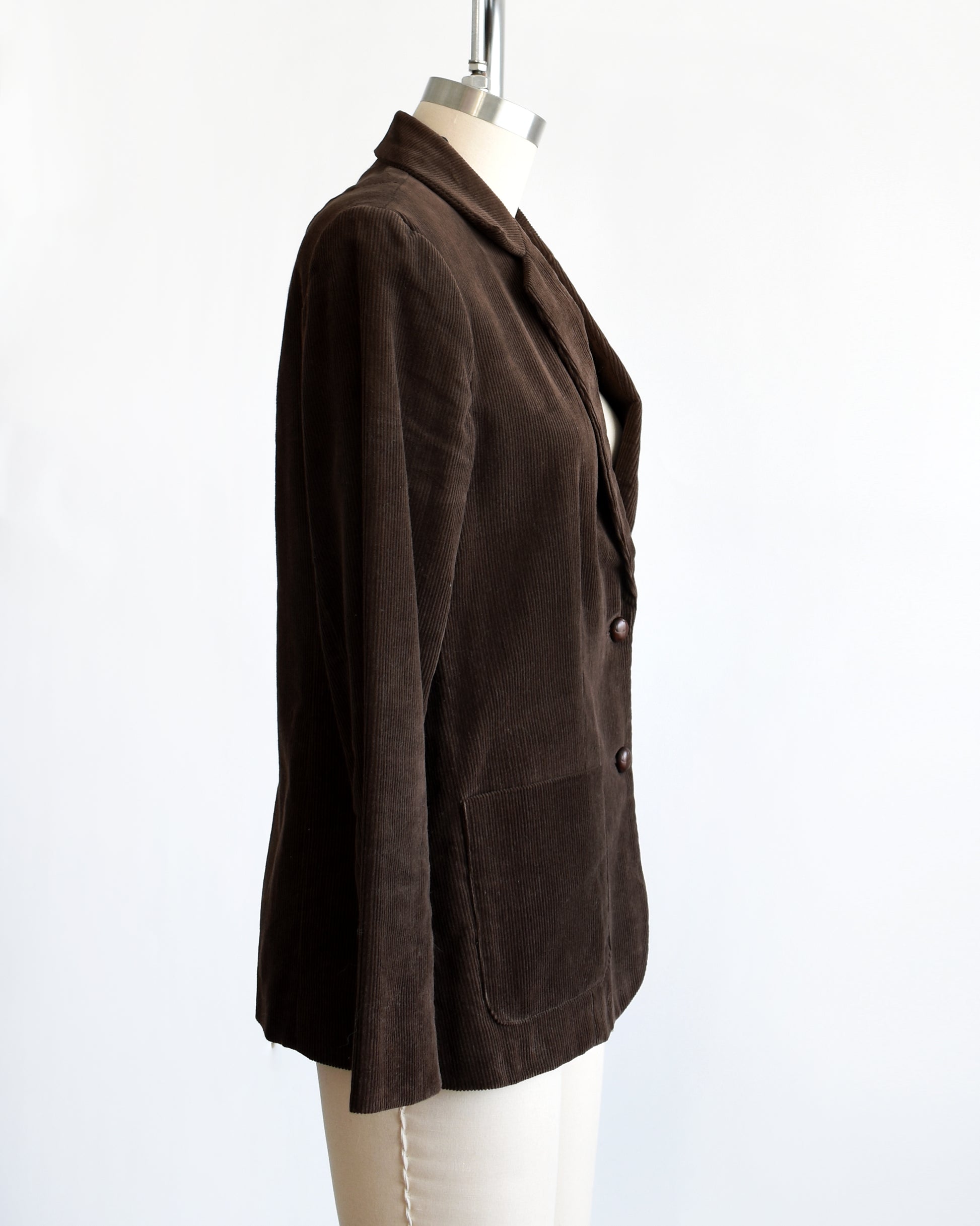 Side view of a vintage 1970s chocolate brown corduroy blazer features two faux wood plastic buttons on the front and two smaller matching buttons on the cuffs.