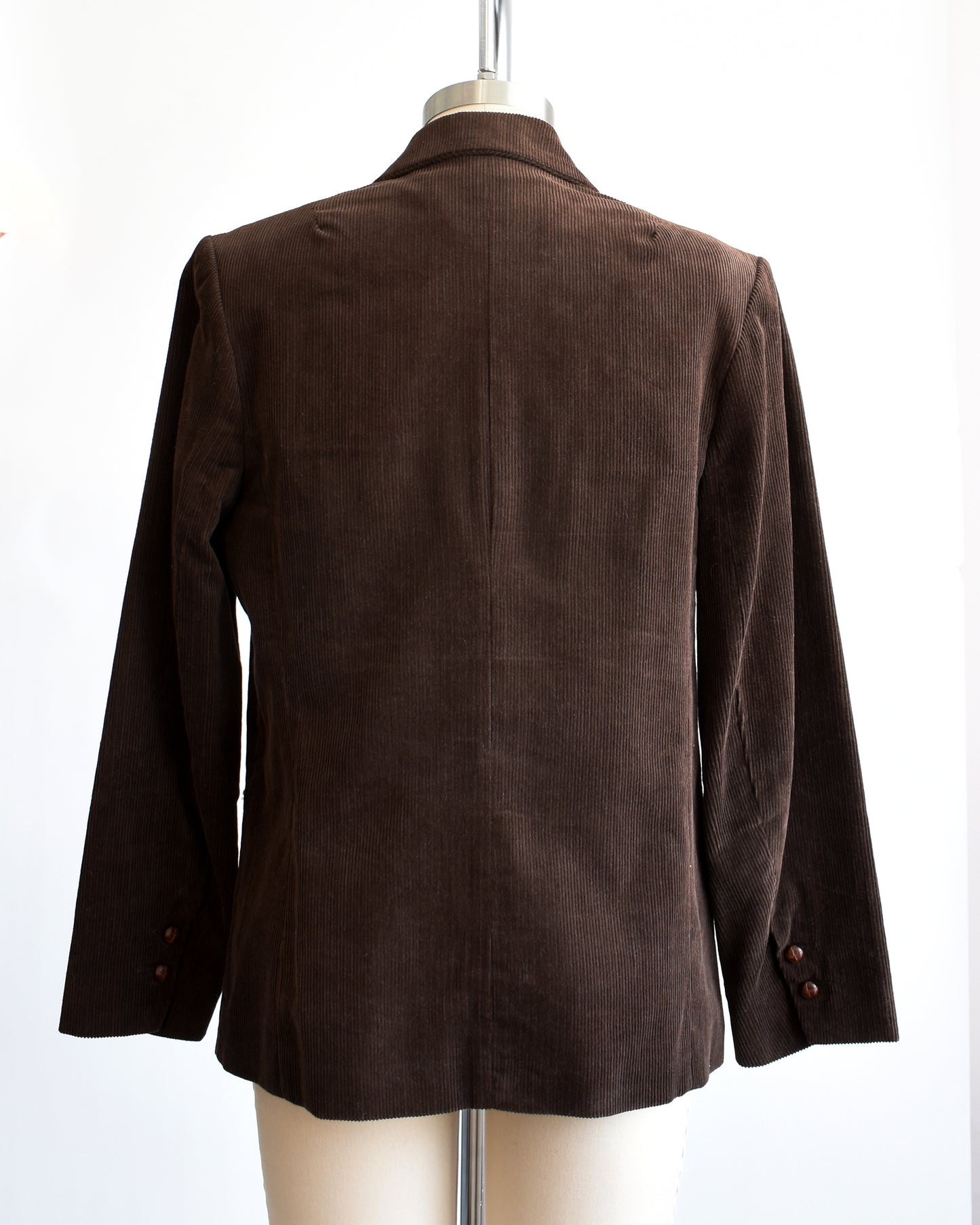 Back view of a vintage 1970s chocolate brown corduroy blazer features two faux wood plastic buttons on the front and two smaller matching buttons on the cuffs.