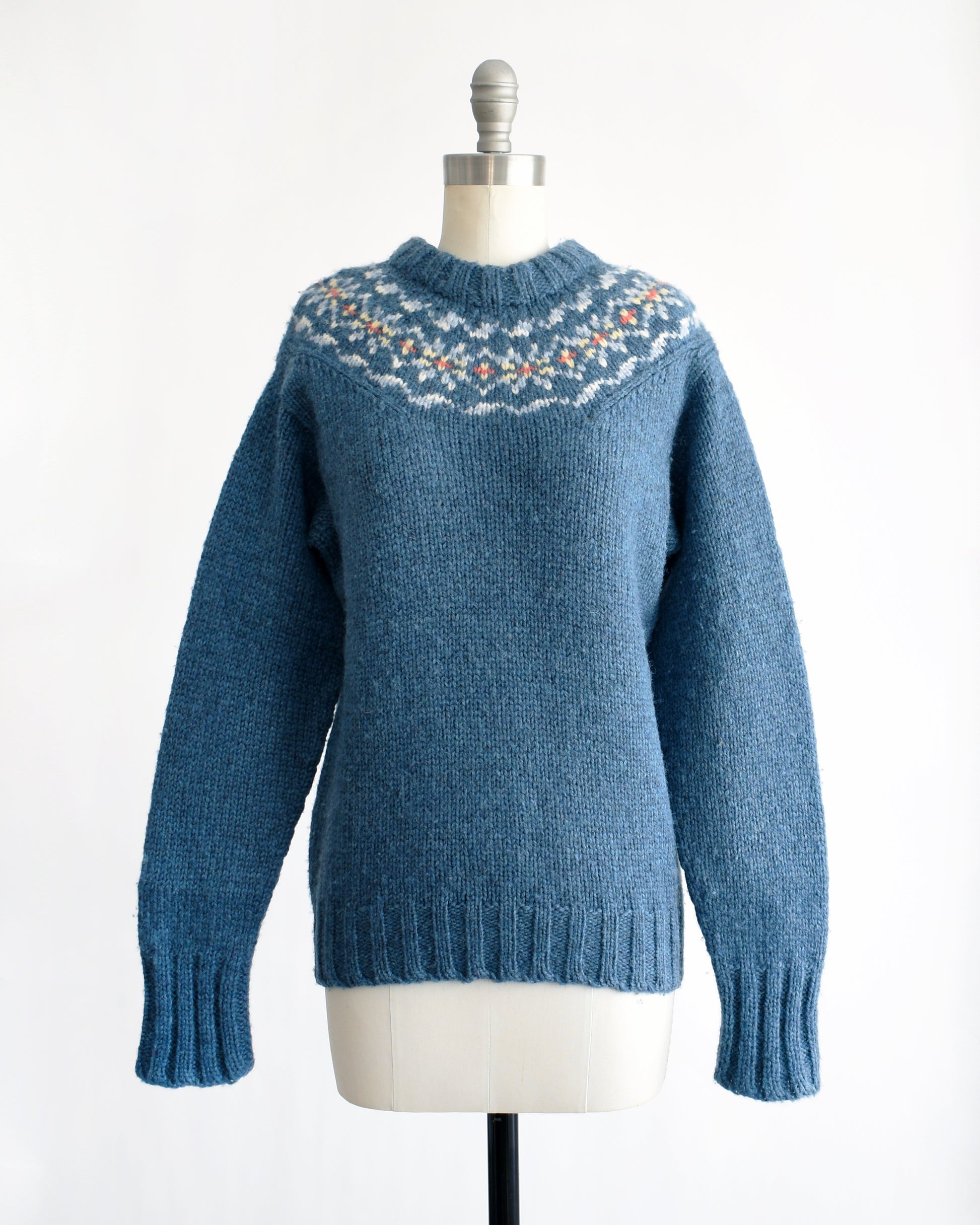 a vintage 1970s blue knitted sweater with patterned yoke on a mannequin against a white background. the sleeves are not cuffed in this photo