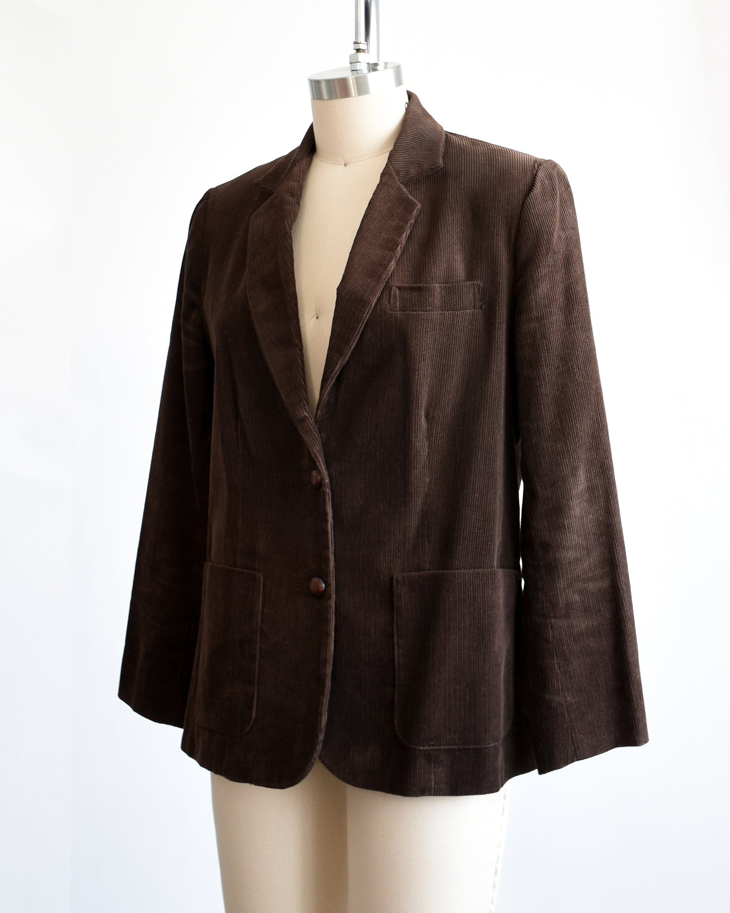 Side front view of a vintage 1970s chocolate brown corduroy blazer features two faux wood plastic buttons on the front and two smaller matching buttons on the cuffs.