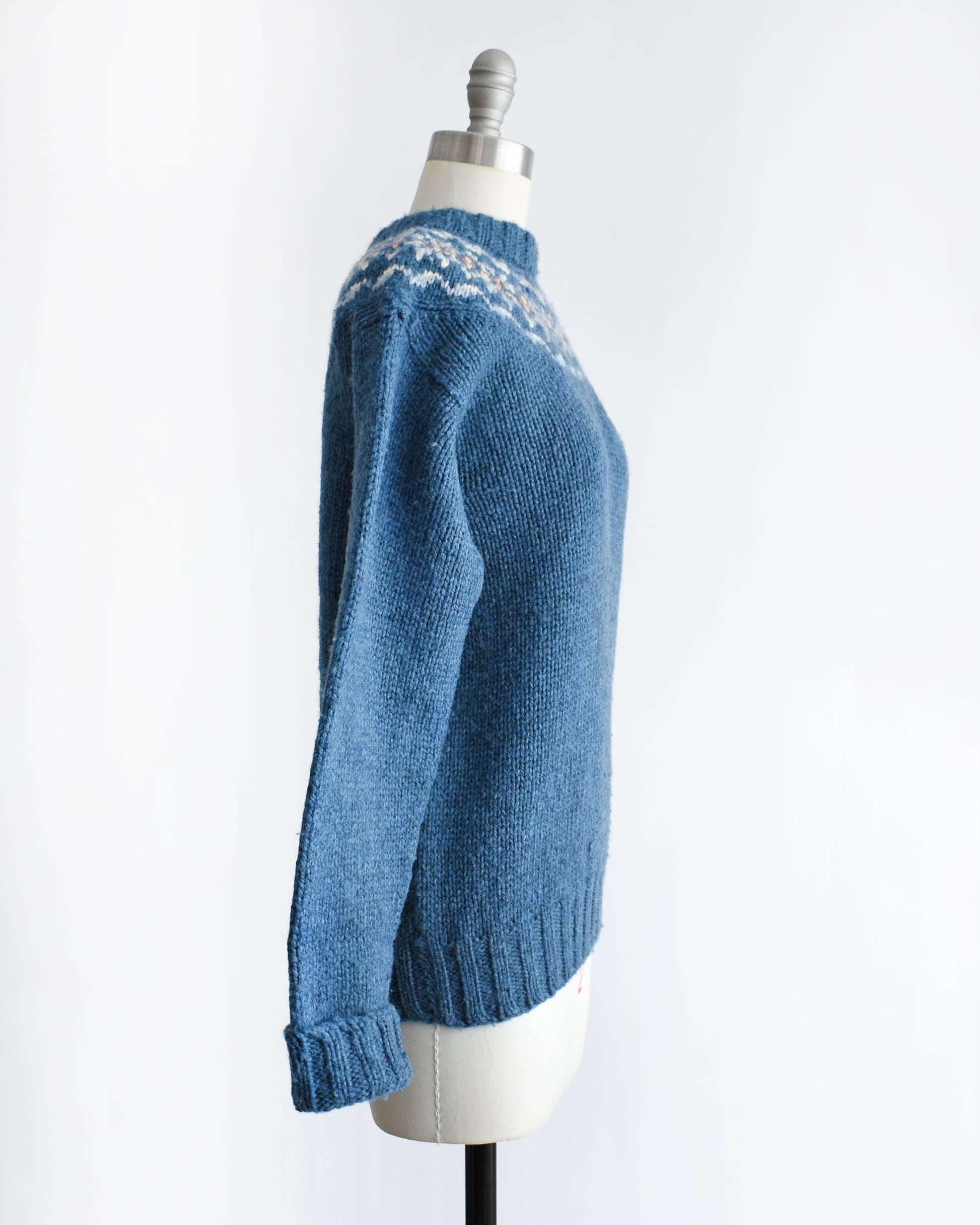 side view of a vintage 1970s blue knitted sweater with patterned yoke on a mannequin against a white background