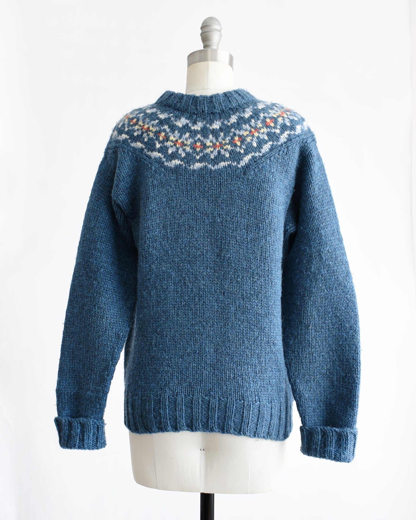 back view of a vintage 1970s blue knitted sweater with patterned yoke on a mannequin against a white background