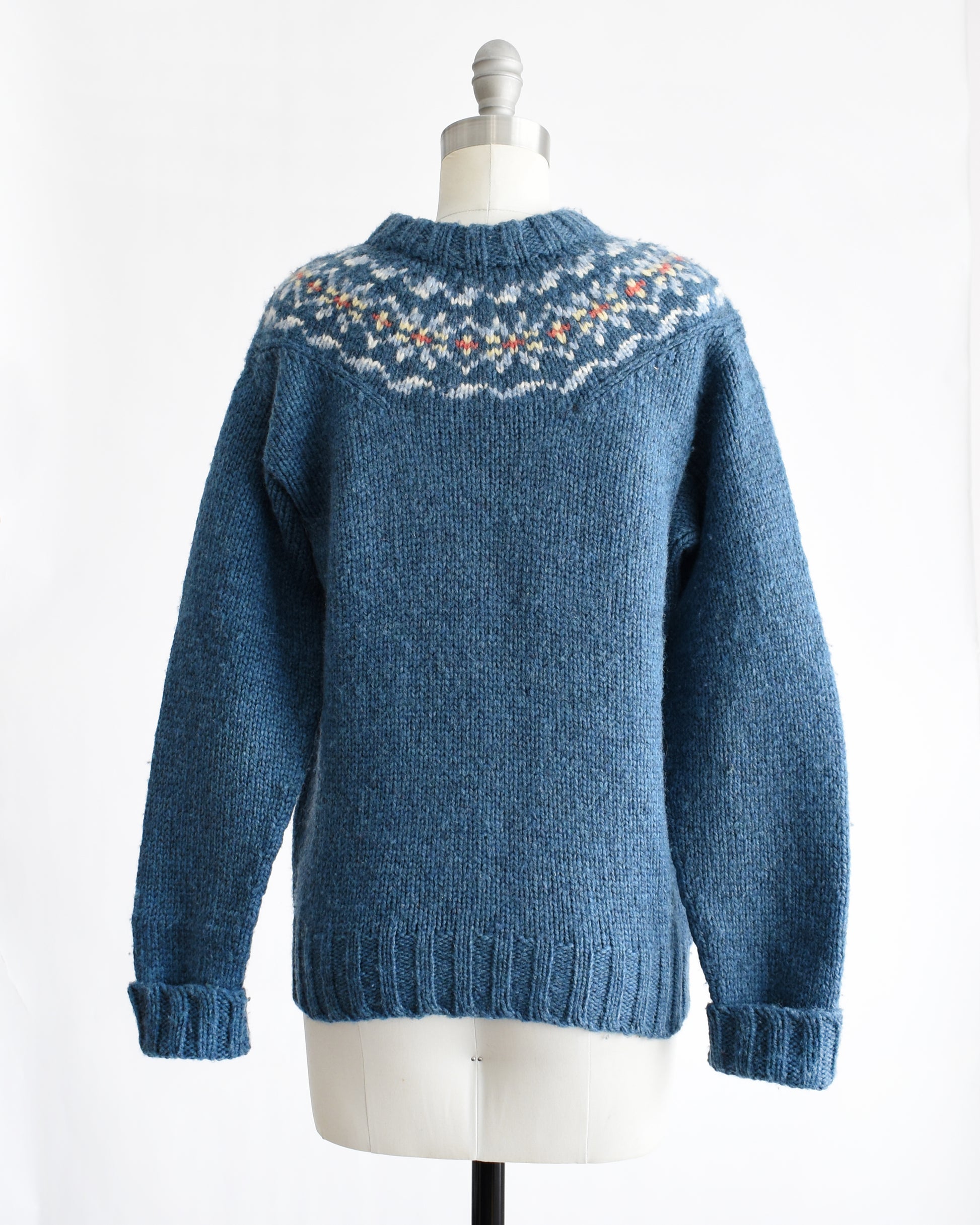 back view of a vintage 1970s blue knitted sweater with patterned yoke on a mannequin against a white background