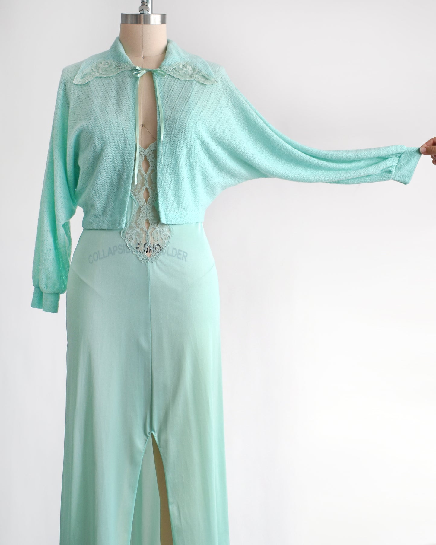 front view of a vintage 1970s mint green nightgown and bed jacket set. The sleeve is being pulled on the bed jacket showing the dolman style sleeve