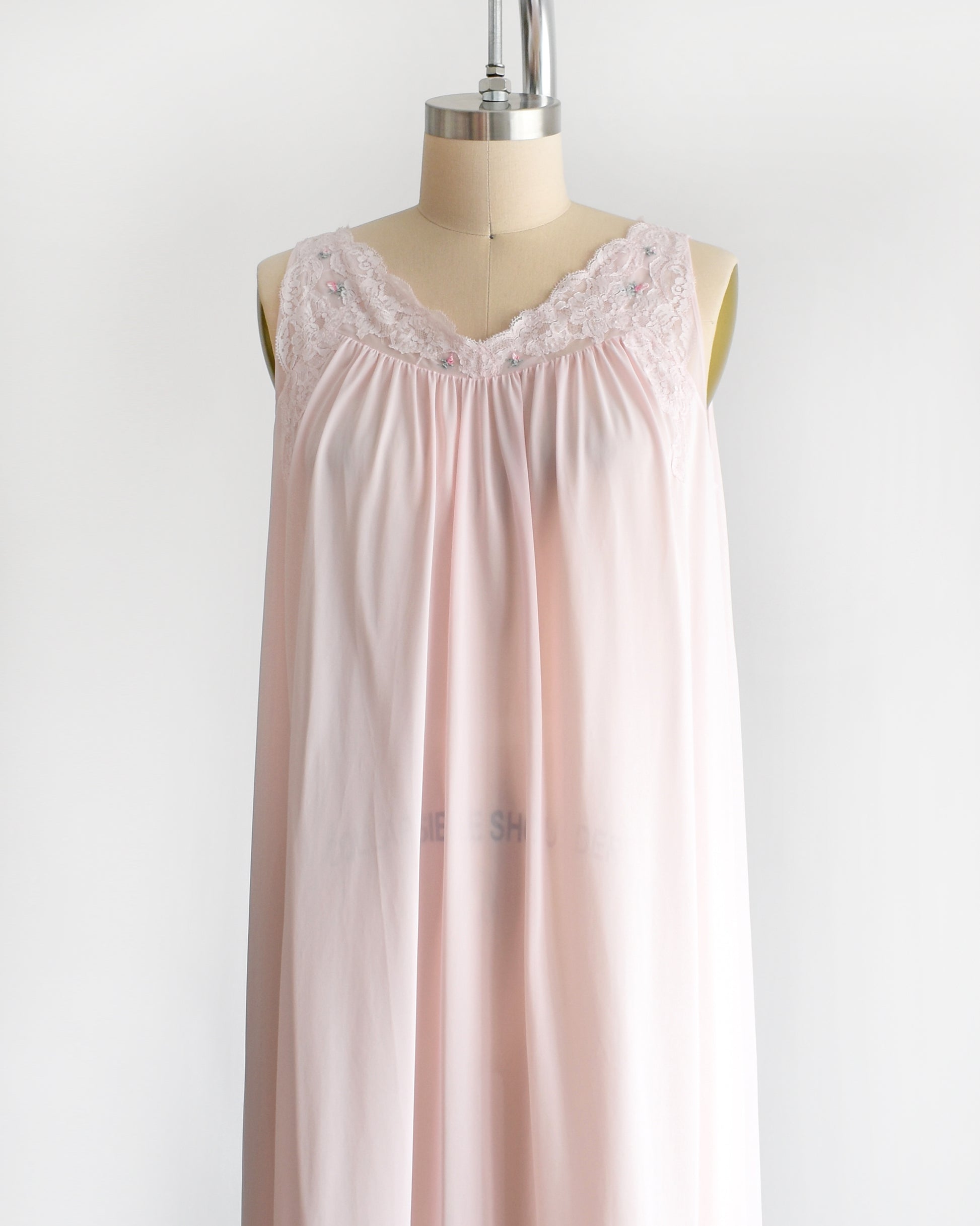 Side front view of a vintage 1970s pink babydoll nightie which has a lace v-neckline that's adorned with lace and has small embroidered flowers on the front.