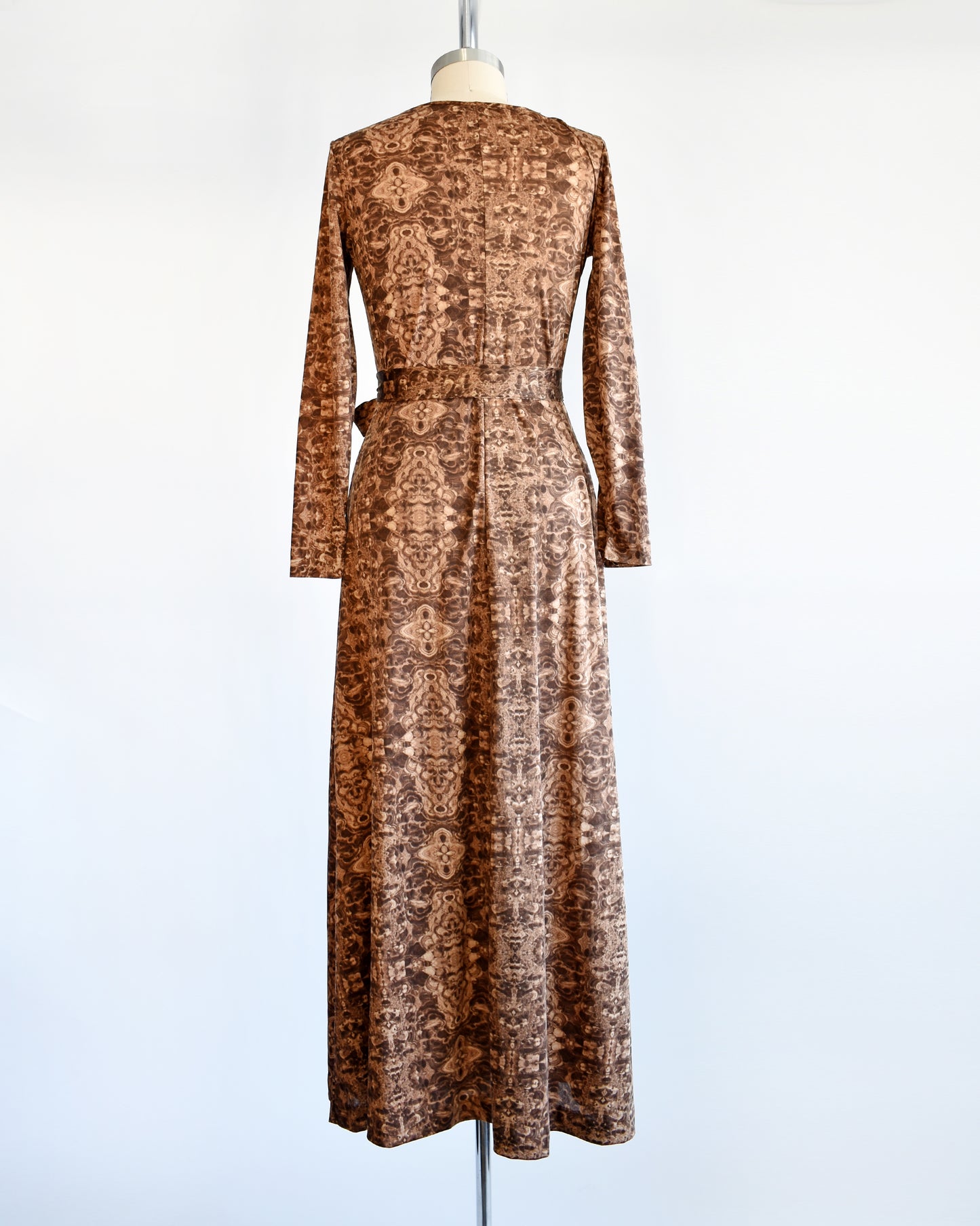 Back view of a vintage 1970s long sleeve maxi dress which features a psychedelic kaleidoscope pattern in light and dark brown.
