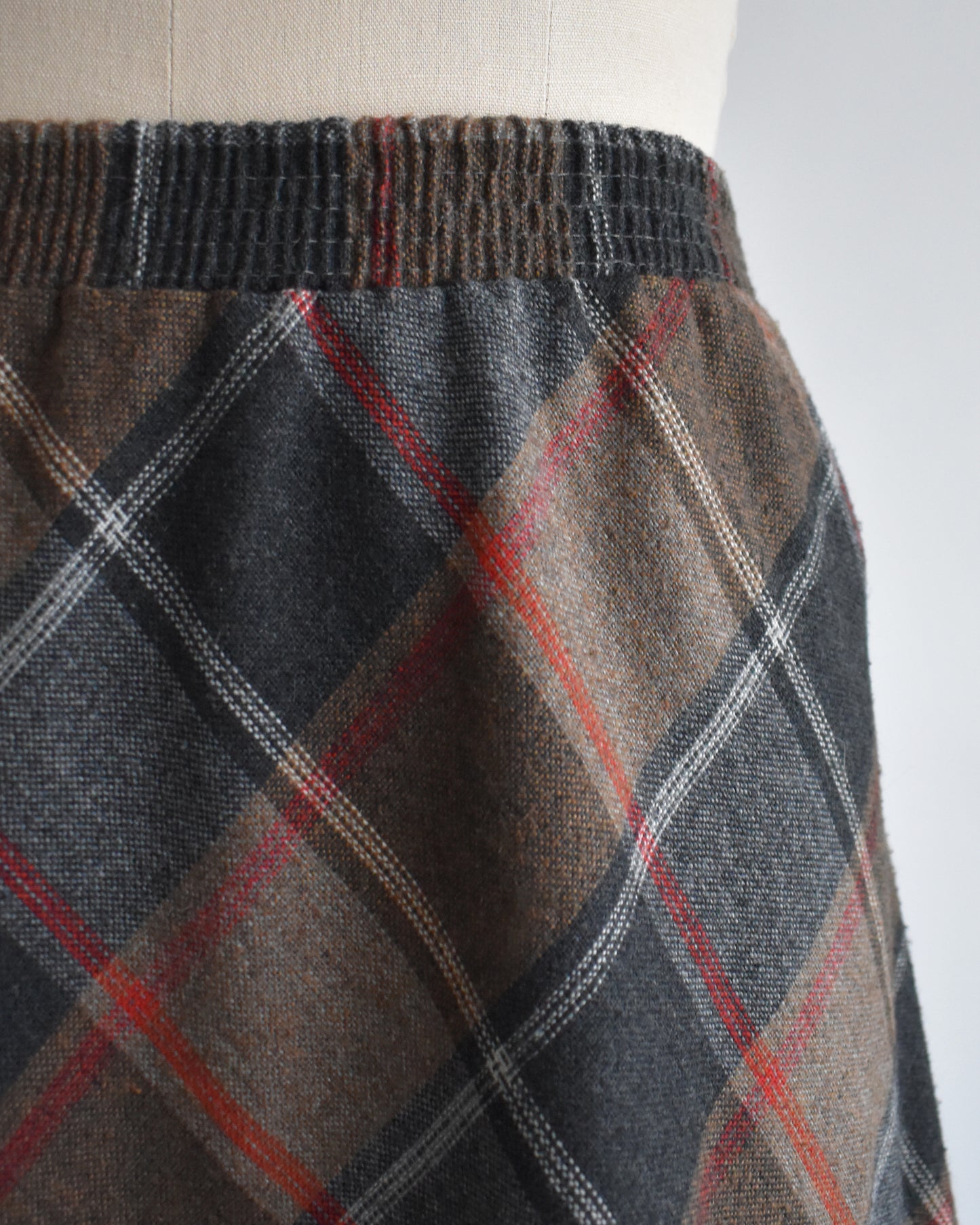 Plaid skirt with brown, red, and gray pattern on a mannequin against a white background