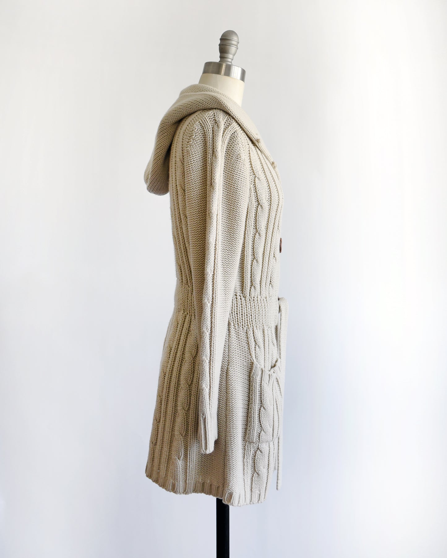 side view of a vintage 1980s beige cable knit cardigan with button details on a mannequin against a white background