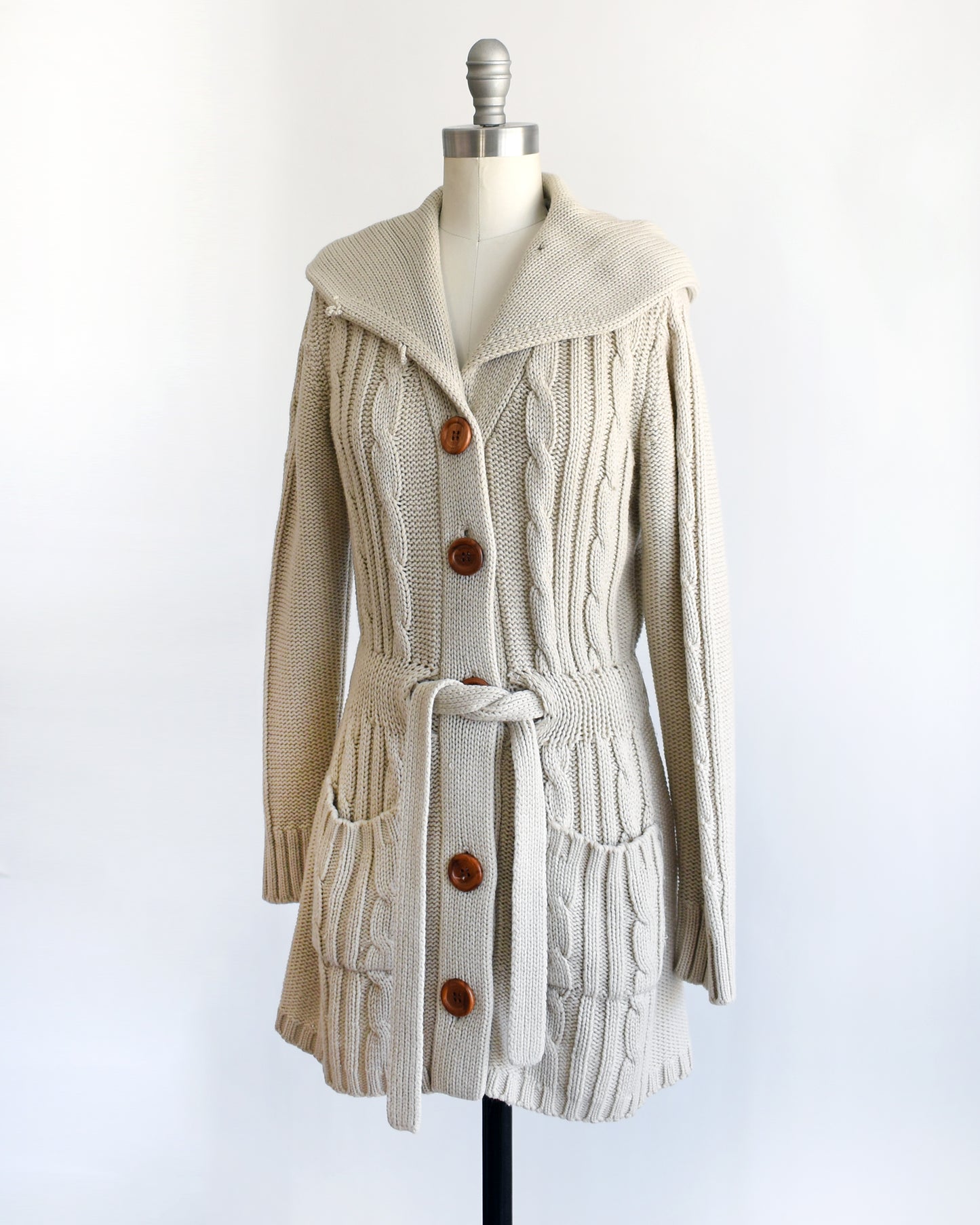 side front view of a vintage 1980s beige cable knit cardigan with button details on a mannequin against a white background