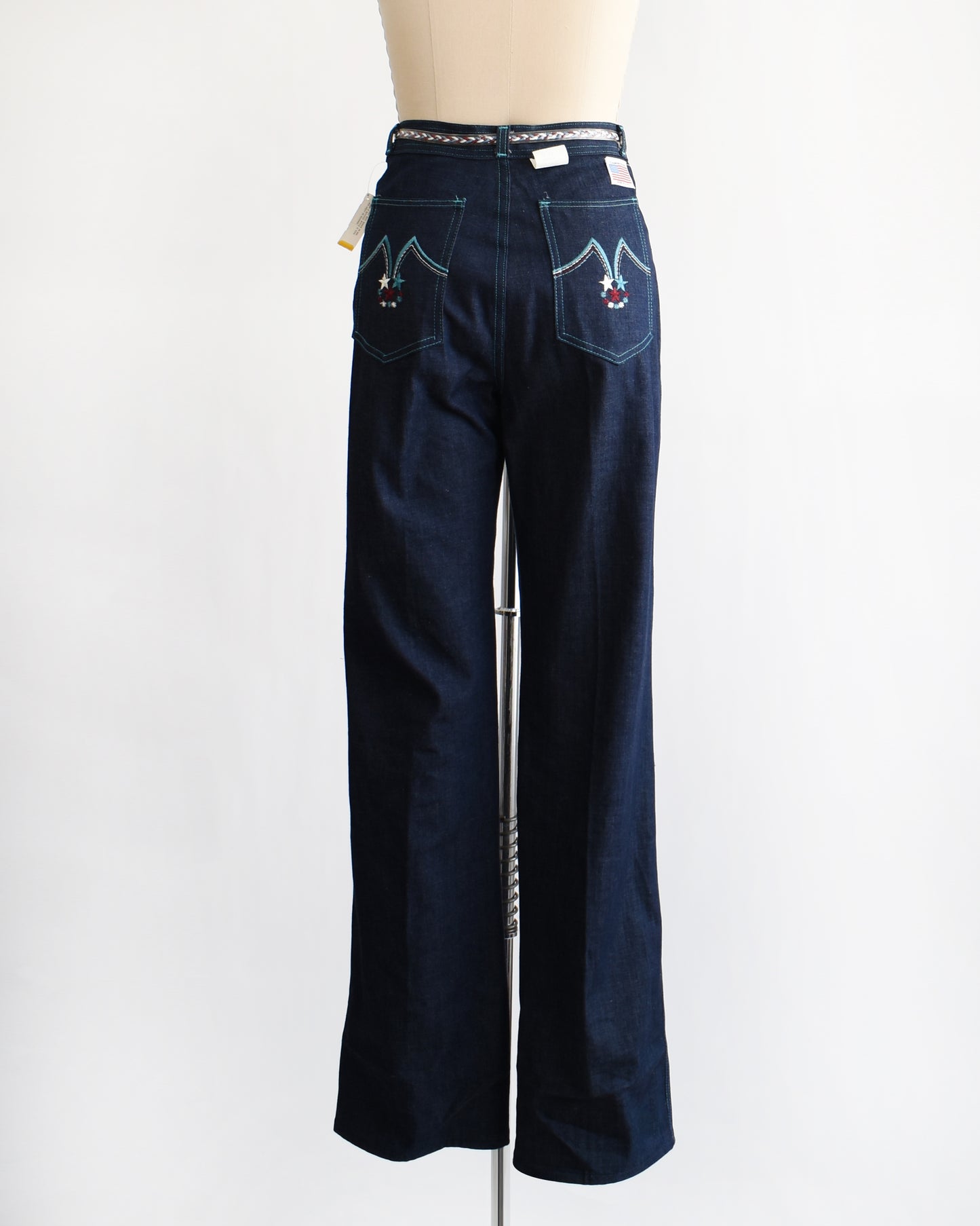 back view of a pair of vintage 1970s dark blue wide leg jeans on a mannequin on a white background