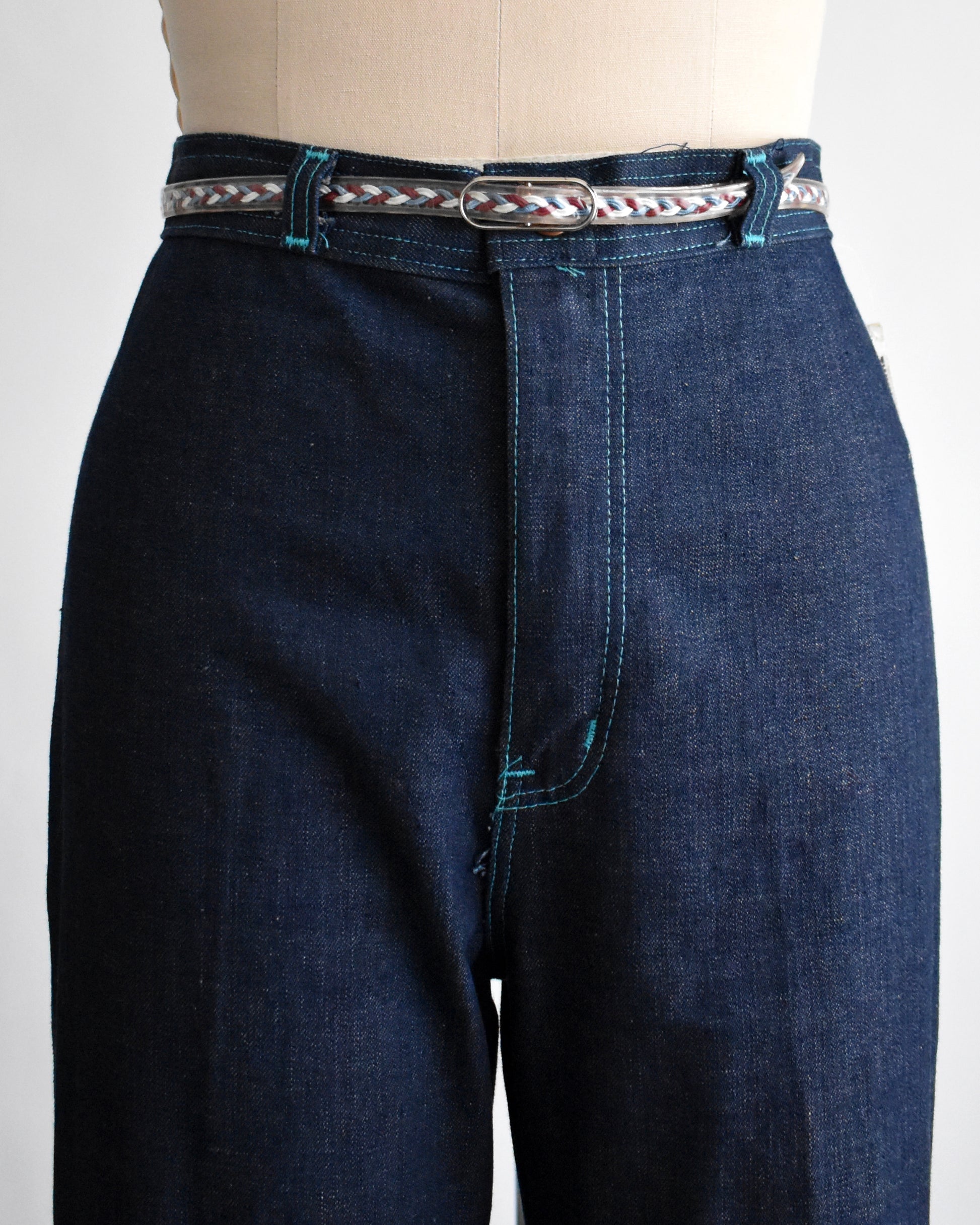 Blue jeans with a decorative belt on a mannequin against a white background