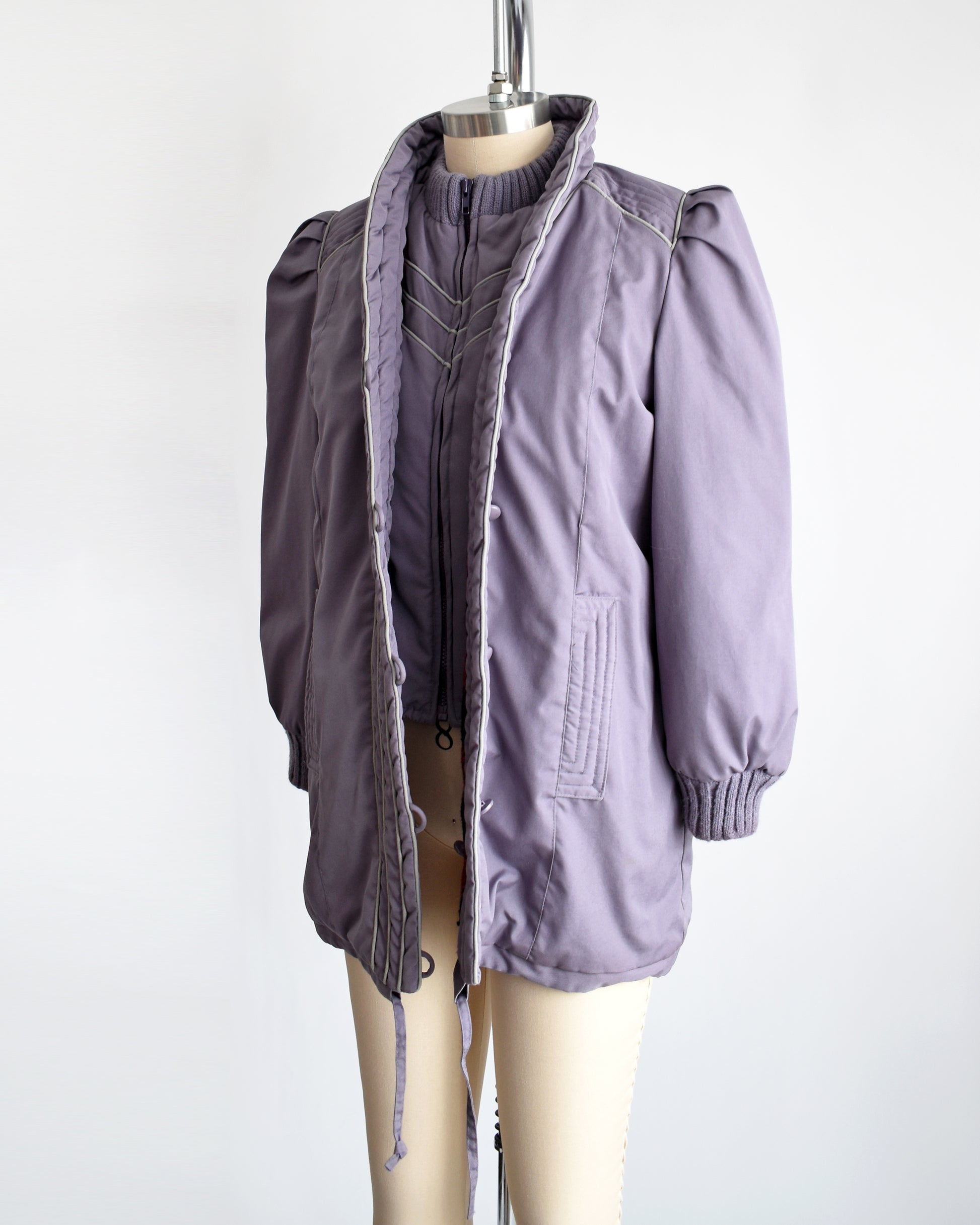   a vintage 1980s purple puffy coat with shawl style collar with gray trim. The coat is unbuttoned in this photo