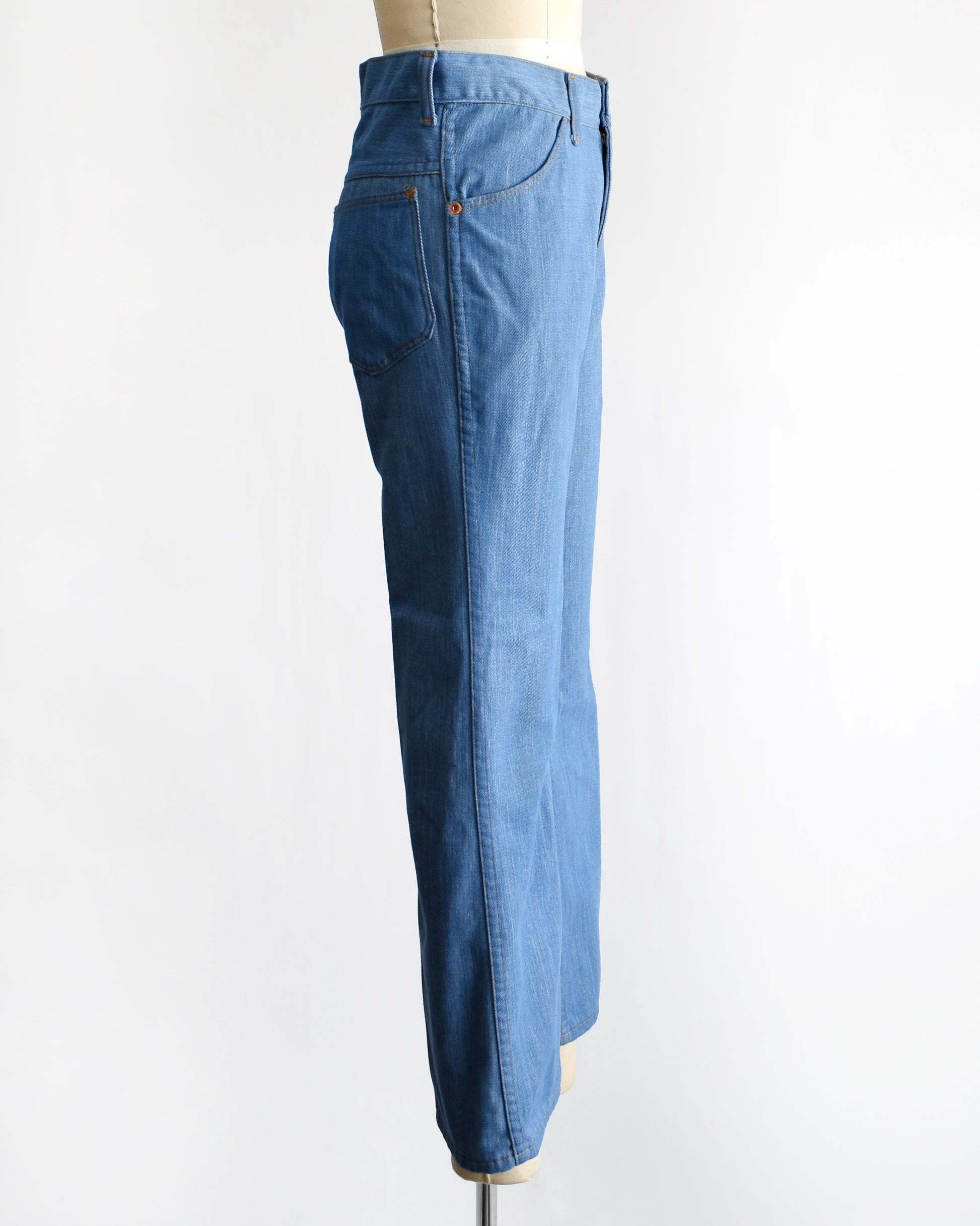 side view of a vintage 1970s pair of bell bottom blue jeans on a mannequin against a white background