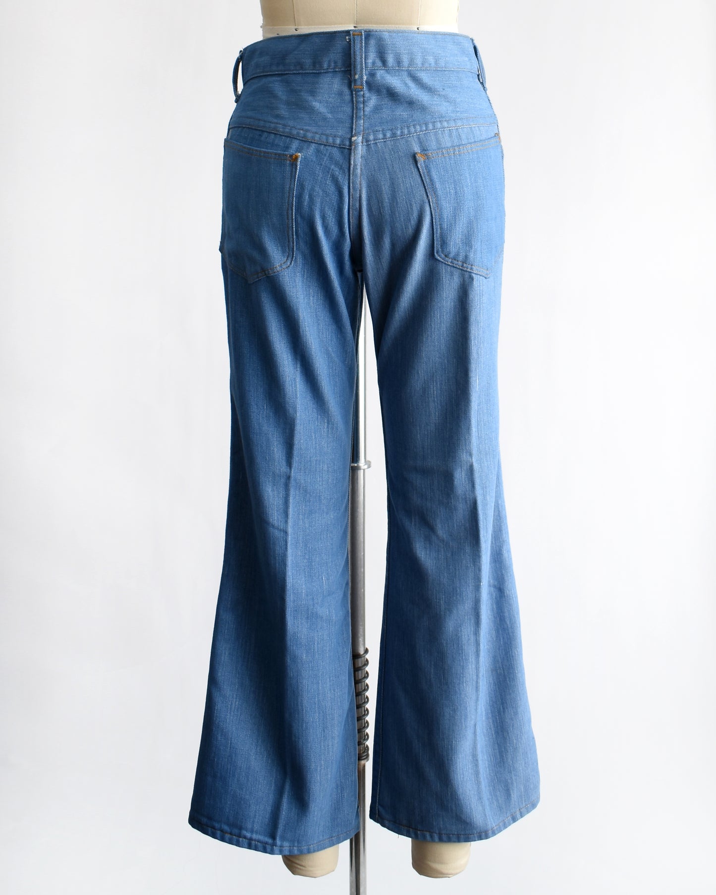 back view of a vintage 1970s pair of bell bottom blue jeans on a mannequin against a white background
