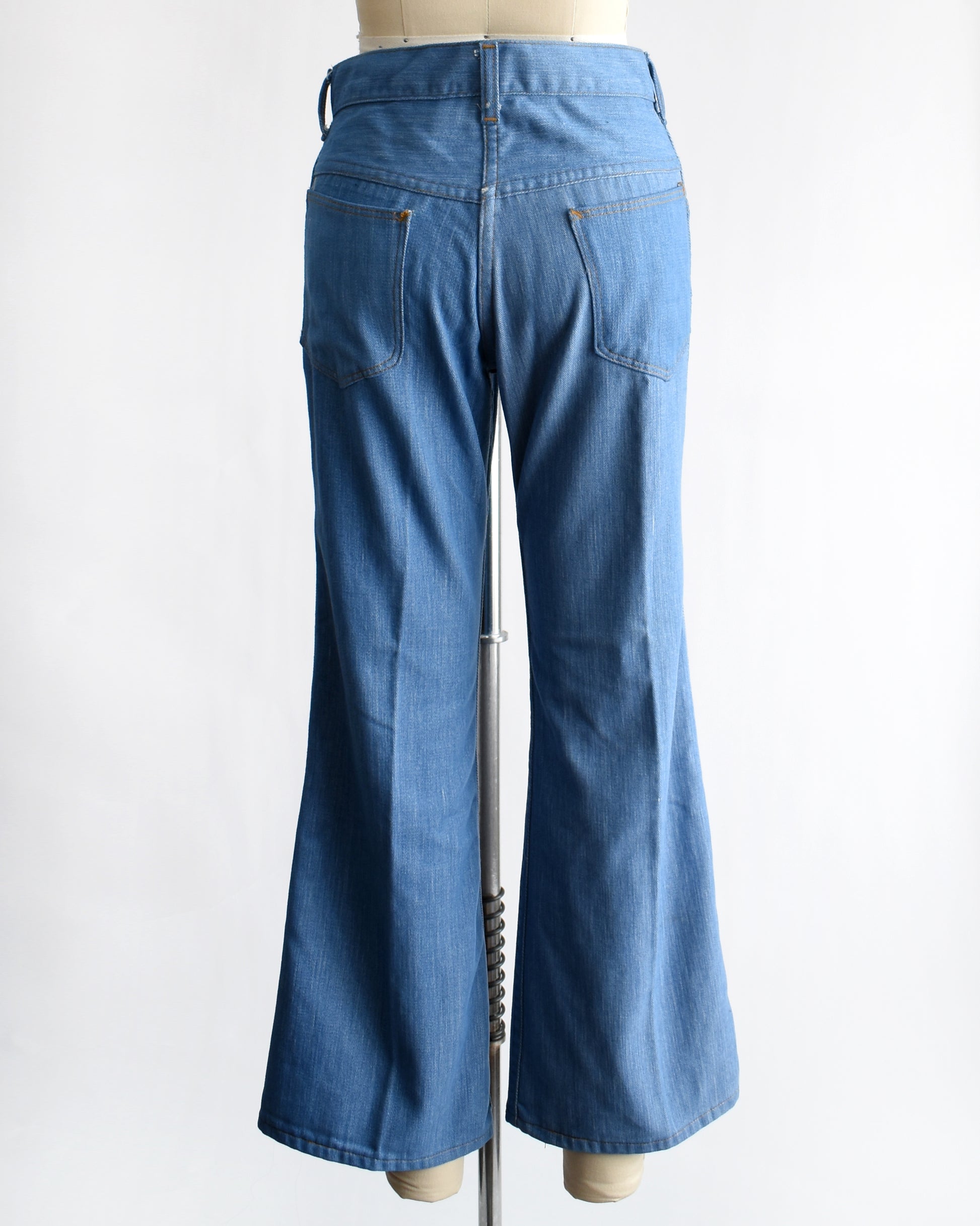 back view of a vintage 1970s pair of bell bottom blue jeans on a mannequin against a white background