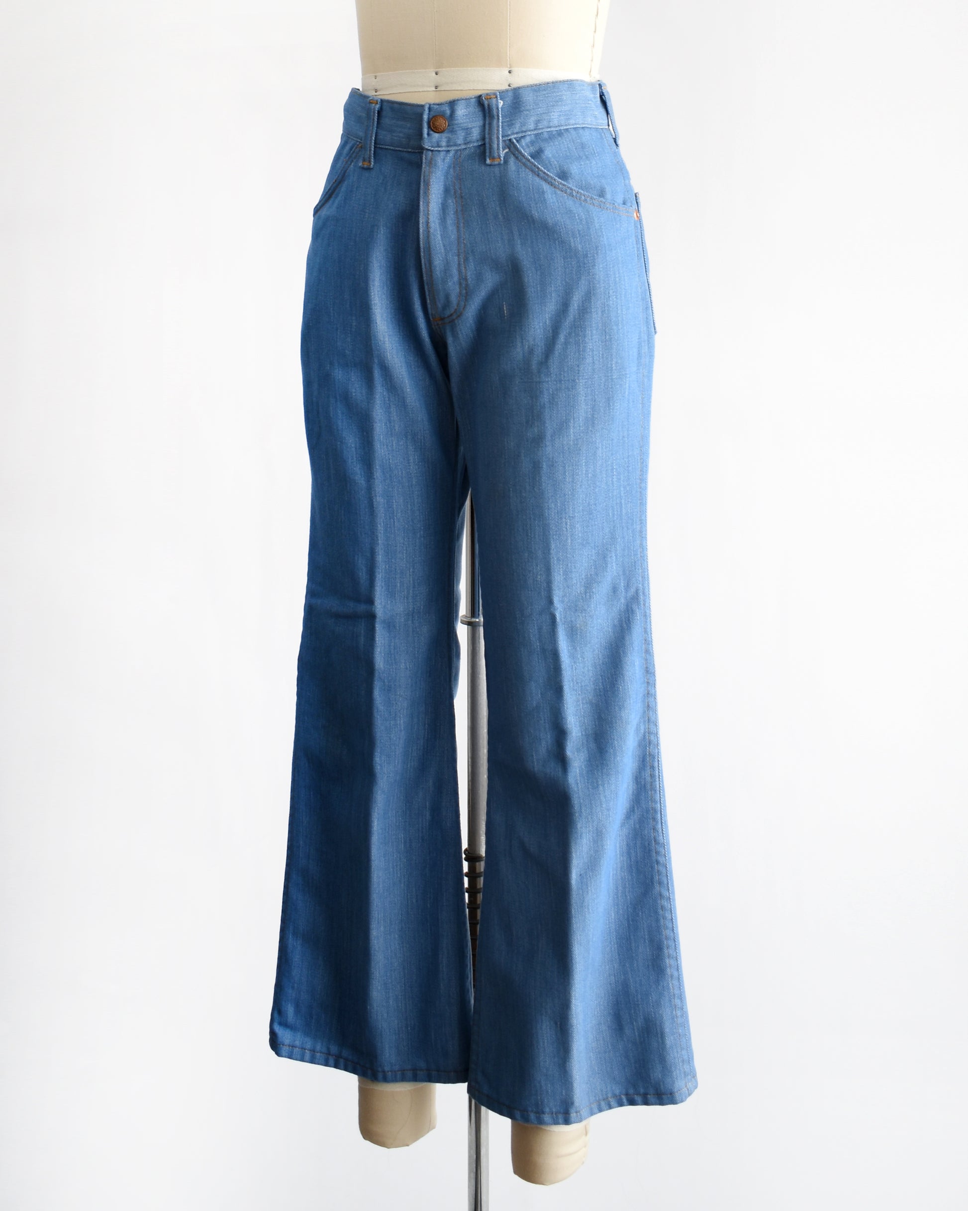 side front view of a vintage 1970s pair of bell bottom blue jeans on a mannequin against a white background