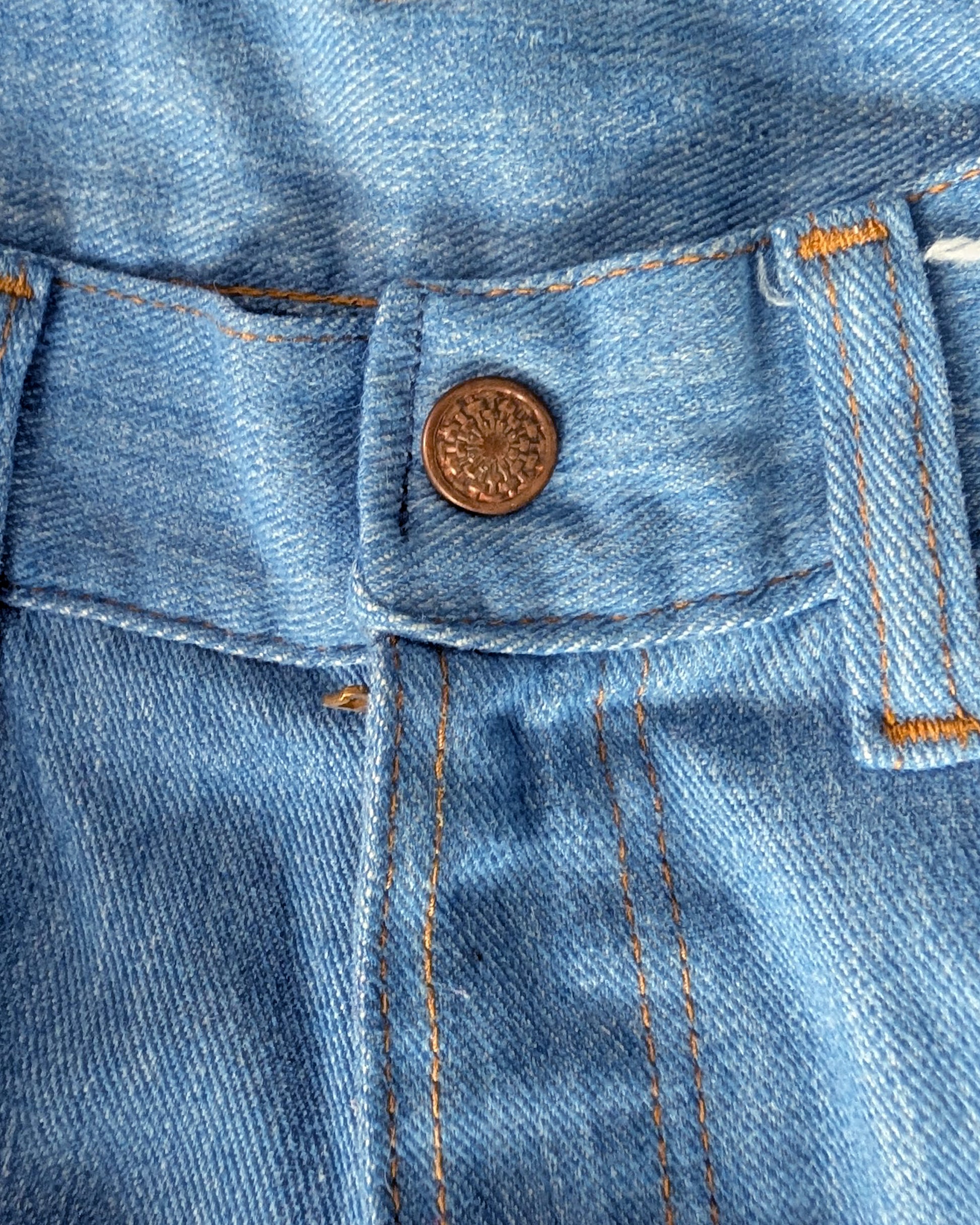 Close-up of a blue denim snap button and stitching details.