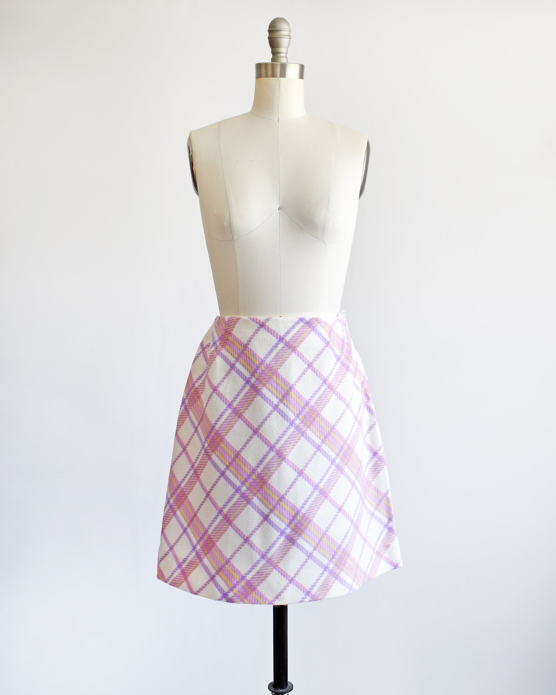 a vintage 1960s pink and purple plaid skirt on a mannequin against a white background