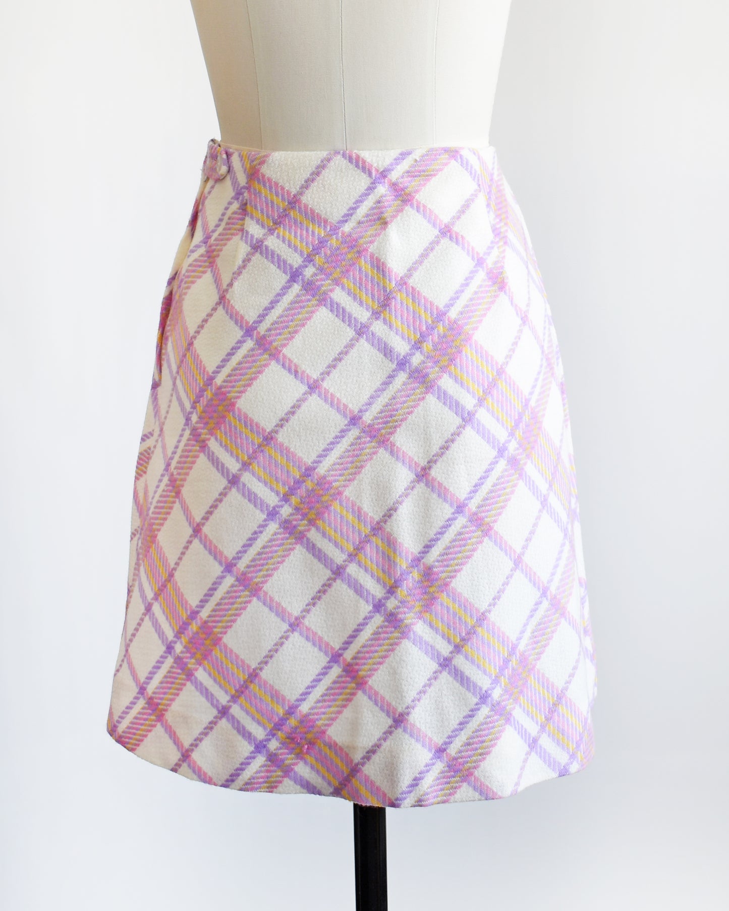 back view of a vintage 1960s pink and purple plaid skirt on a mannequin against a white background