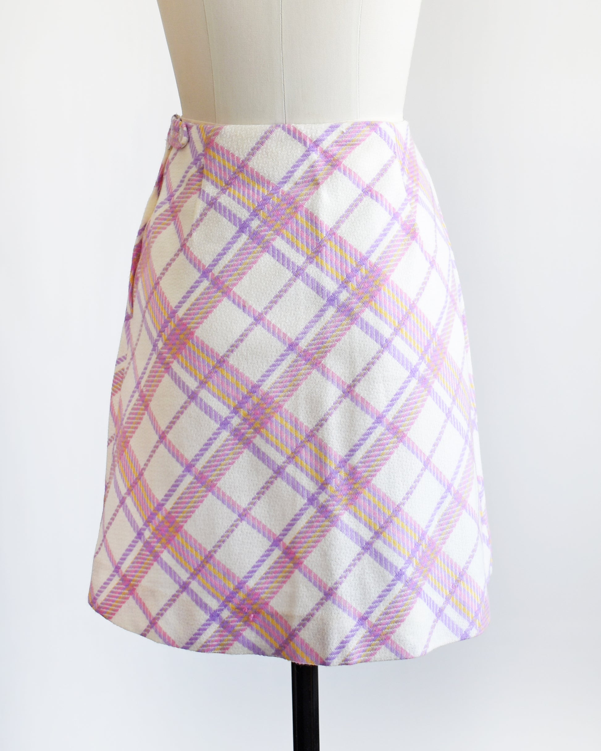 back view of a vintage 1960s pink and purple plaid skirt on a mannequin against a white background