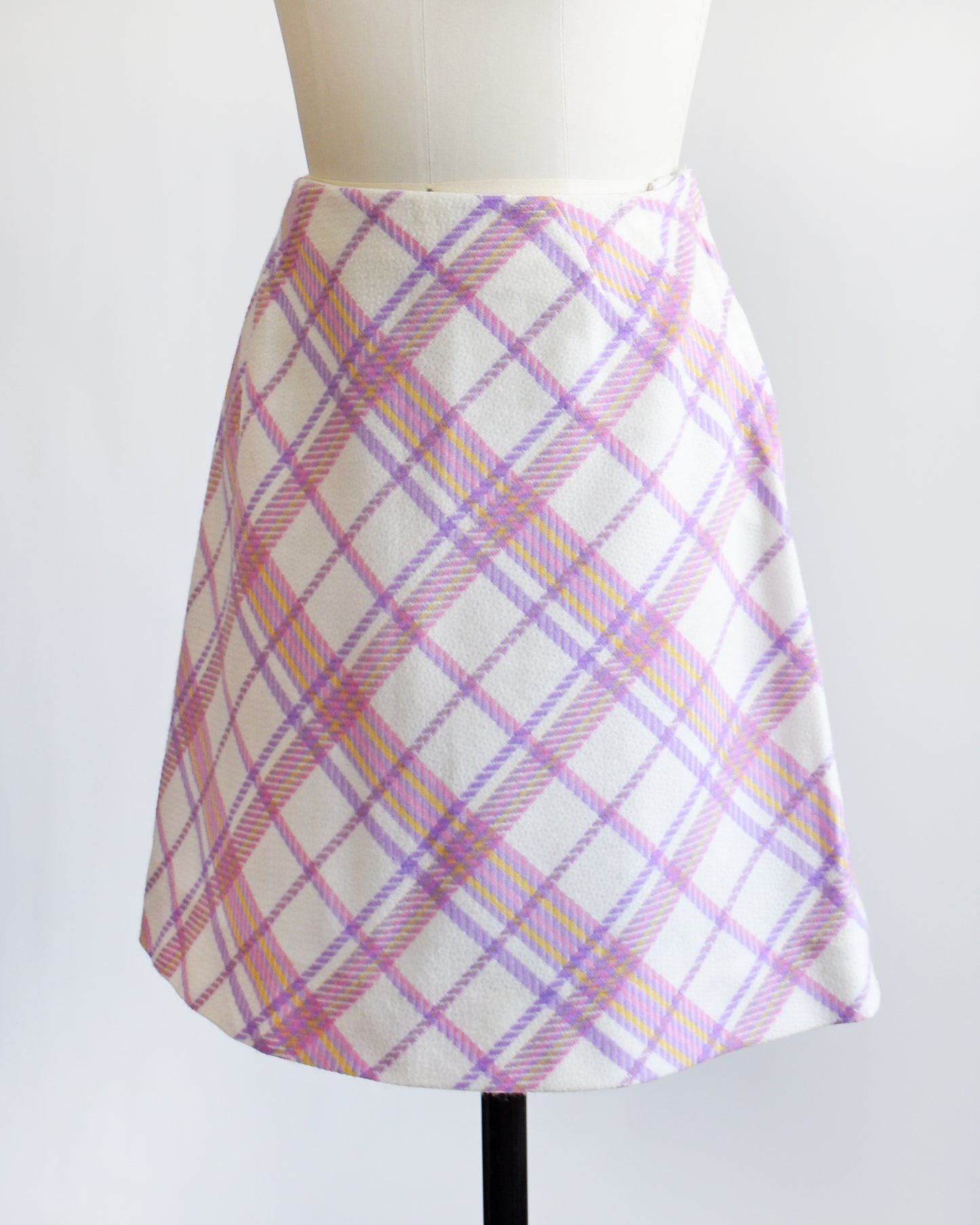 side front view of a vintage 1960s pink and purple plaid skirt on a mannequin against a white background