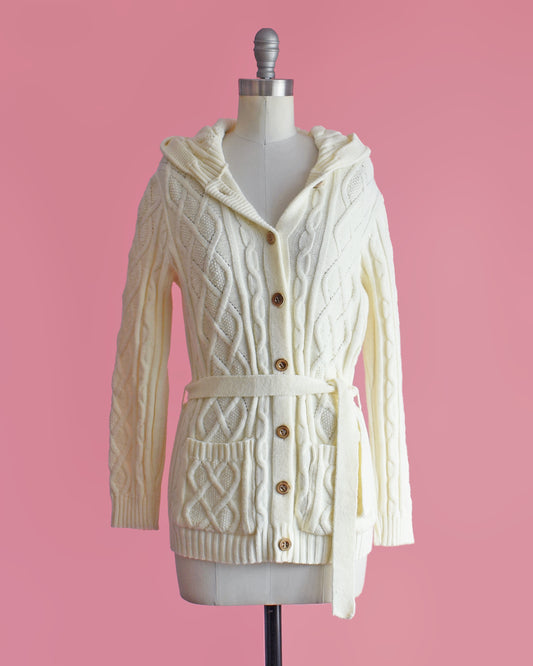 a vintage 1970s cream-colored cable knit hooded cardigan on a mannequin against a pink background