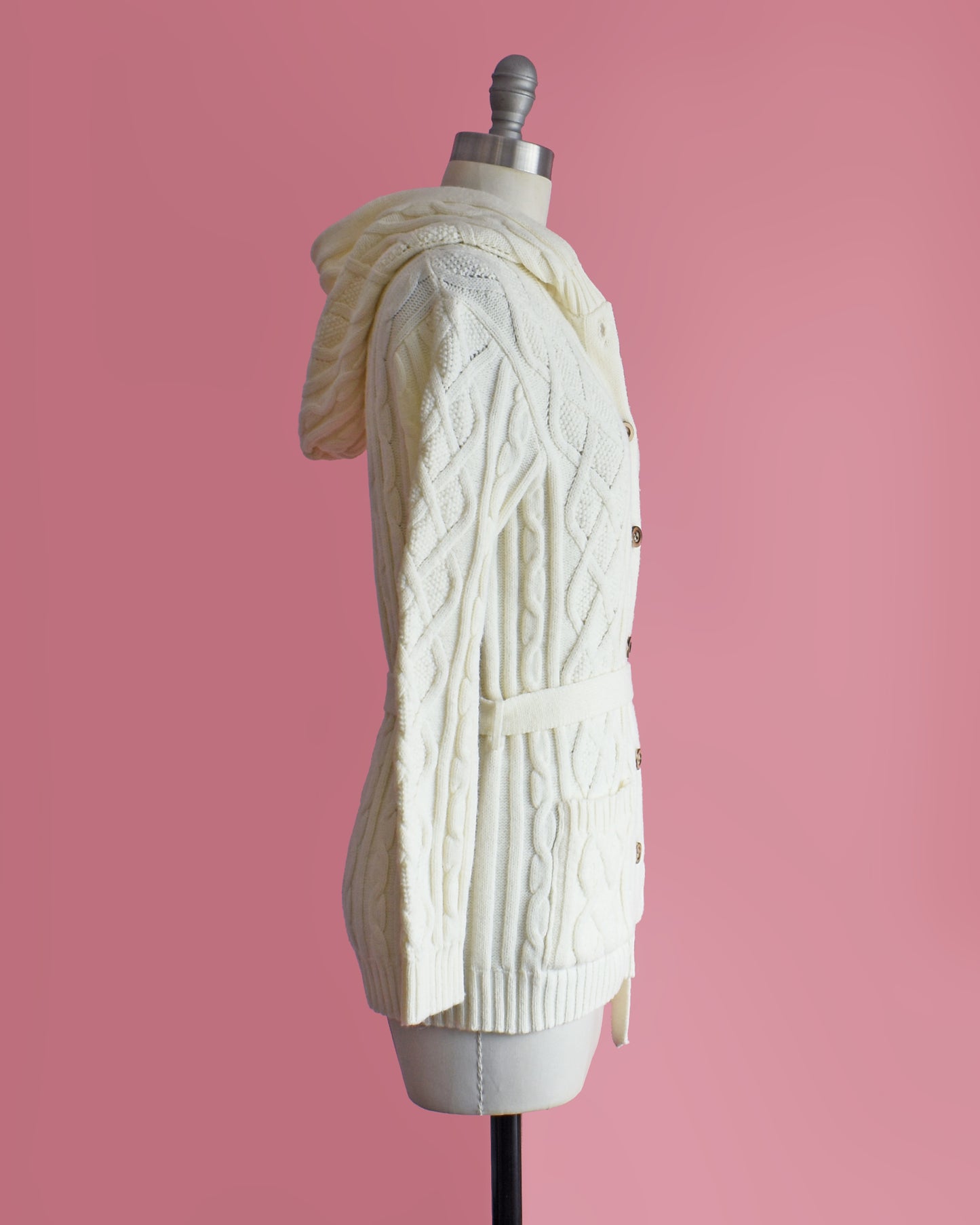 side view of a vintage 1970s cream-colored cable knit hooded cardigan on a mannequin against a pink background