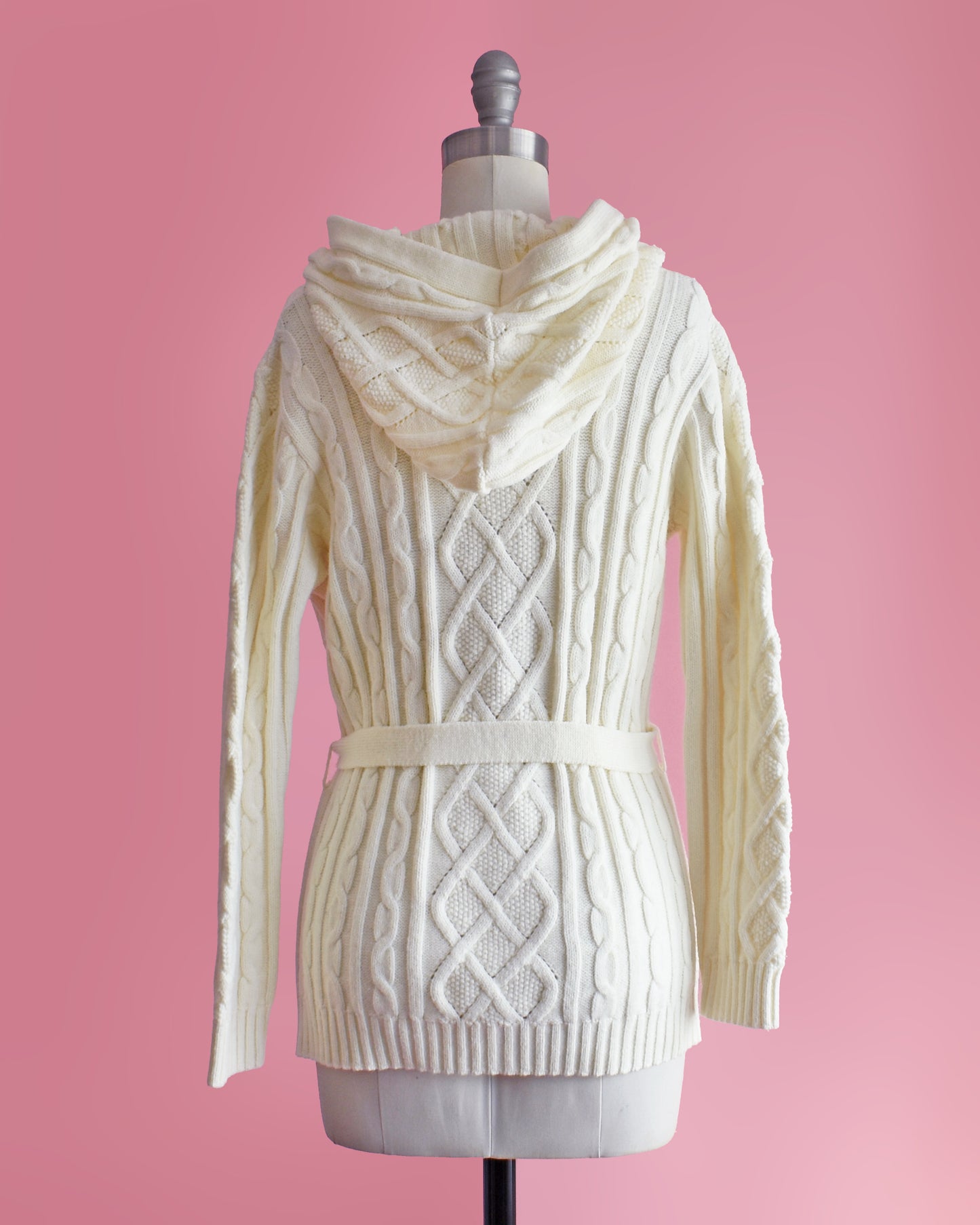 back view of side view of a vintage 1970s cream-colored cable knit hooded cardigan on a mannequin against a pink background
