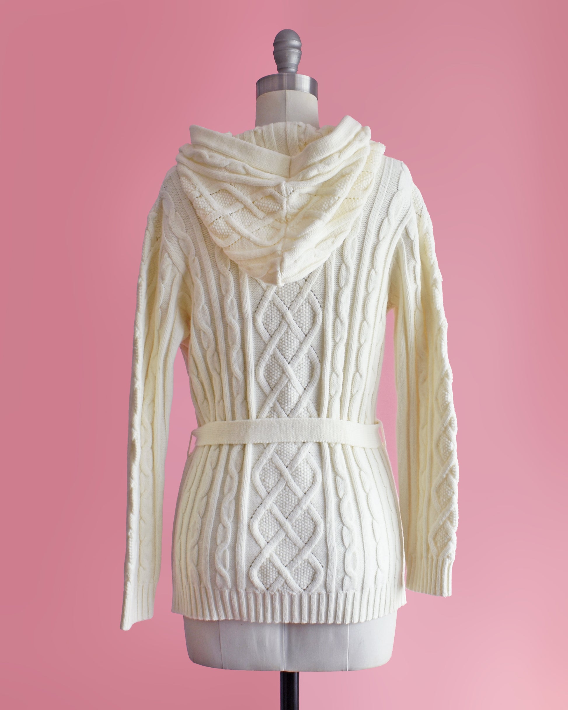 back view of side view of a vintage 1970s cream-colored cable knit hooded cardigan on a mannequin against a pink background