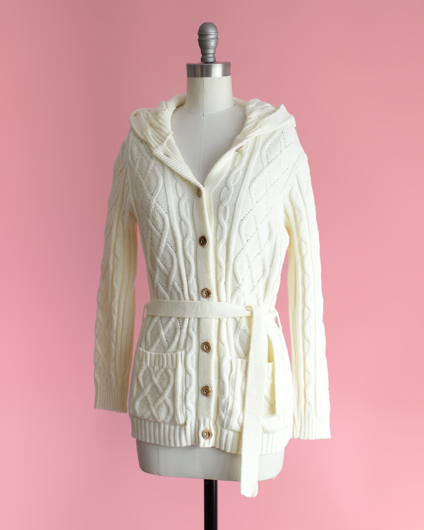 side front view of side view of a vintage 1970s cream-colored cable knit hooded cardigan on a mannequin against a pink background