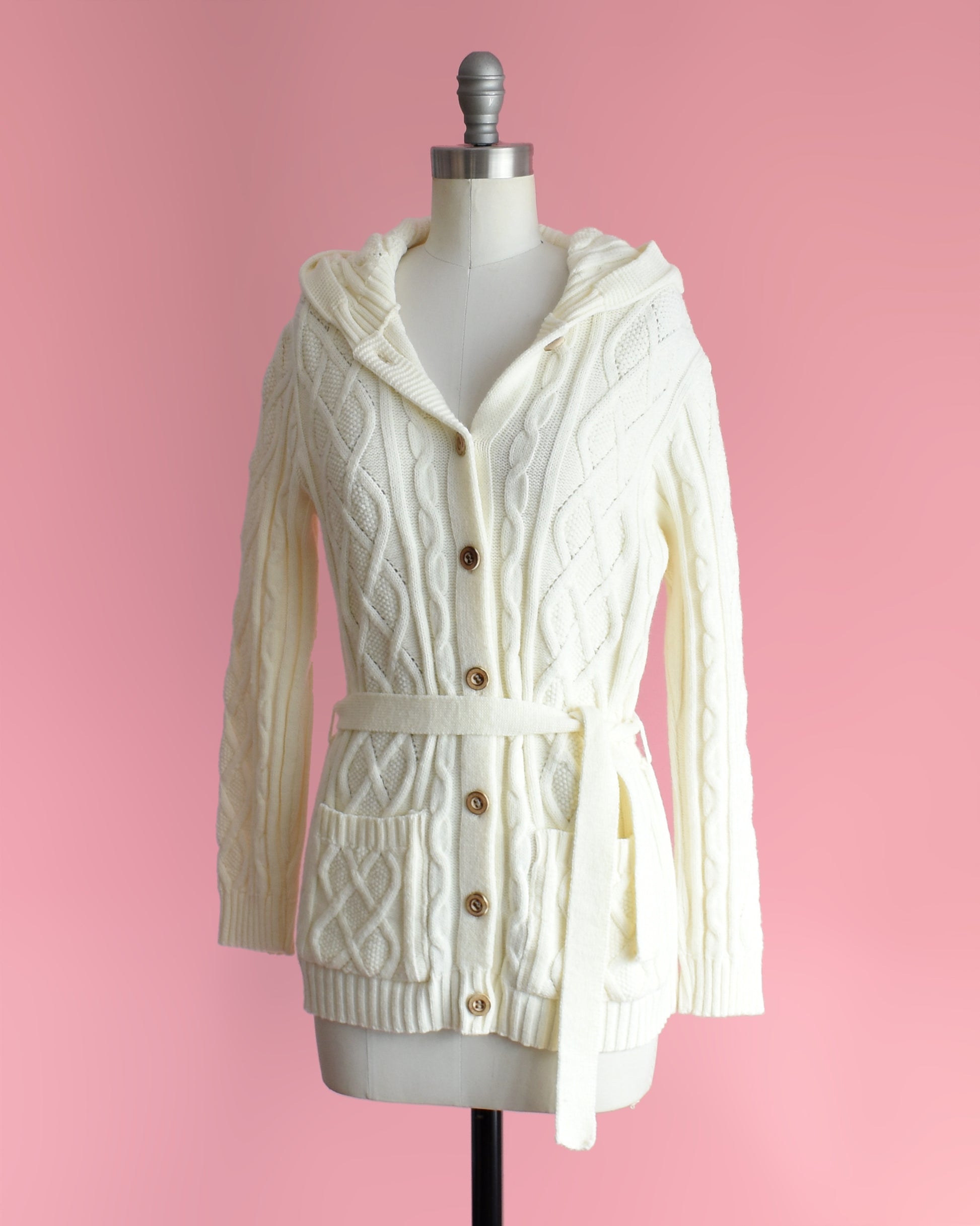 side front view of side view of a vintage 1970s cream-colored cable knit hooded cardigan on a mannequin against a pink background