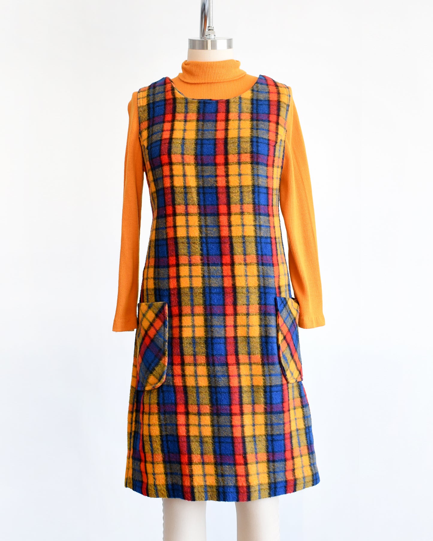 A vintage 1970s orange, blue, and red plaid pinafore dress with an orange turtleneck underneath