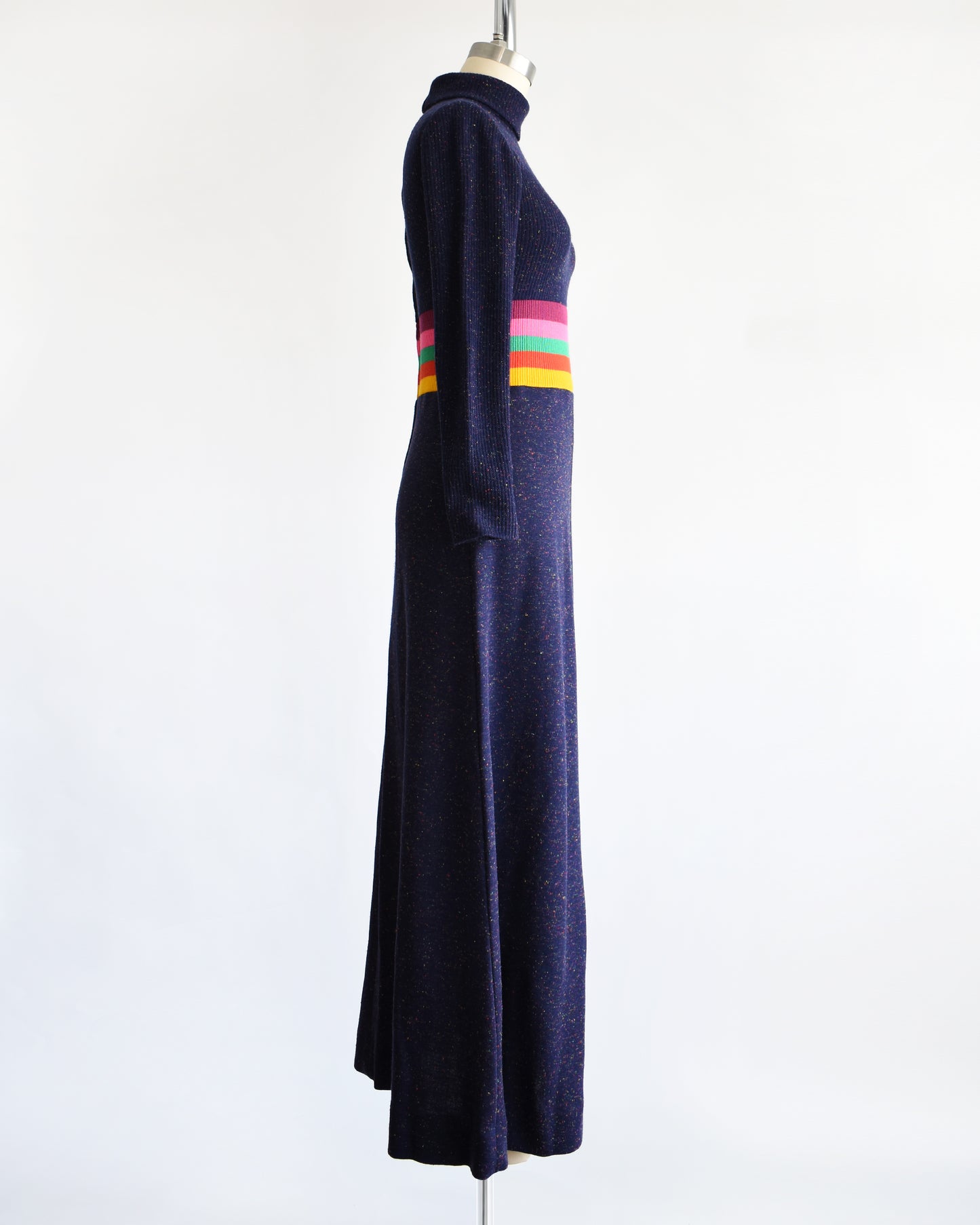 side view of a vintage 1970s purple blue dress with a colorful striped waistband on a mannequin against a white background
