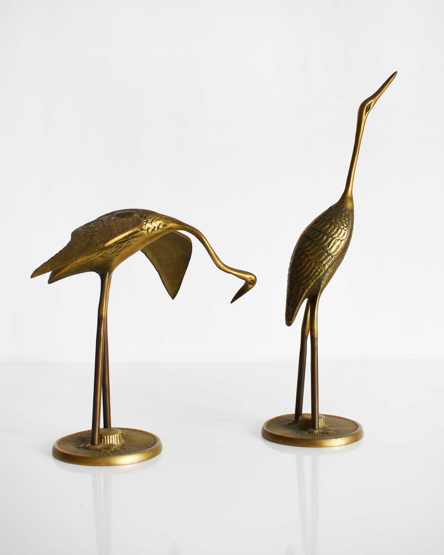 Side view of a pair of vintage brass cranes that have ornate carved detail on their wings and body.