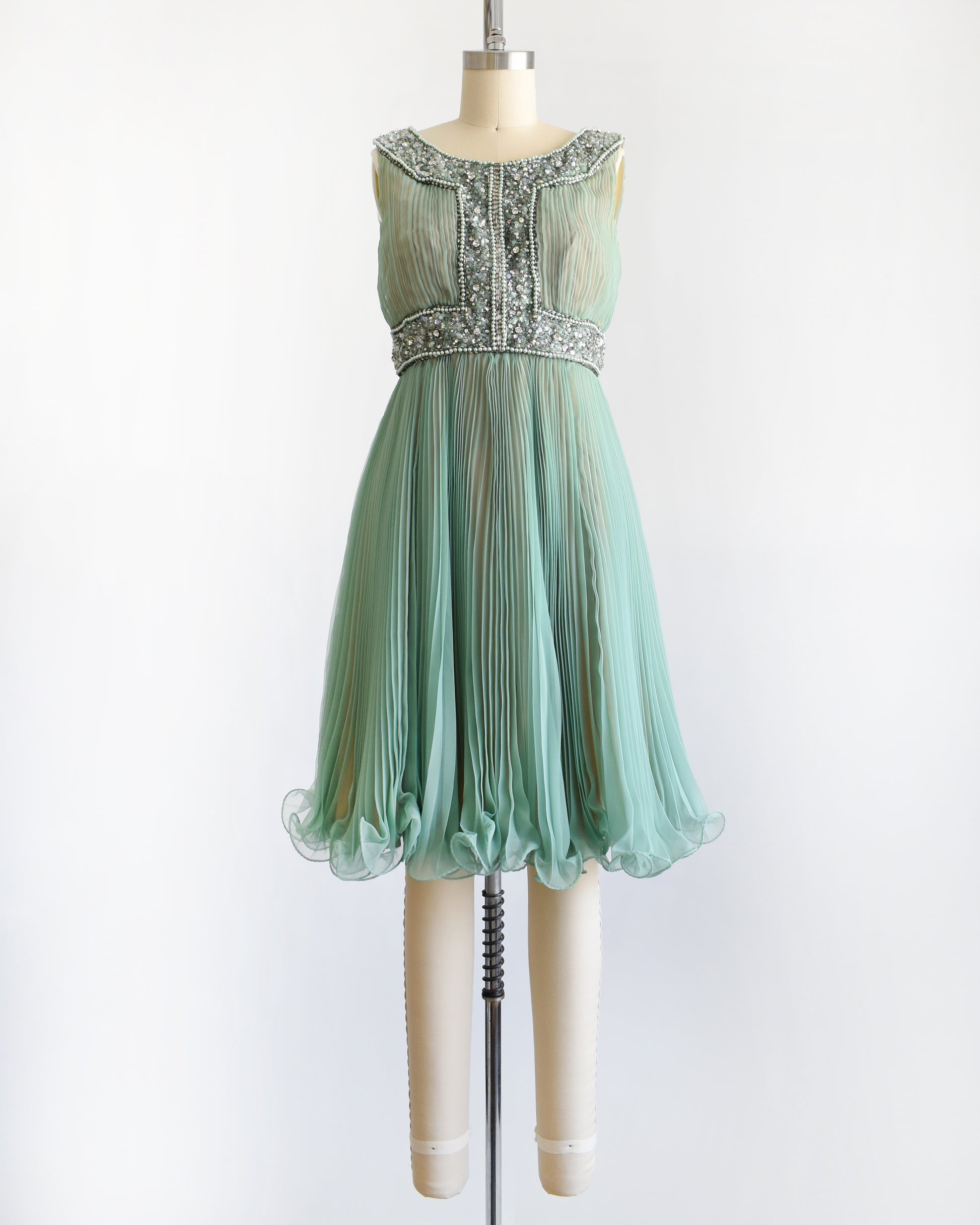 a vintage 1960s green chiffon dress with beaded neckline and bodice on a mannequin against a white background